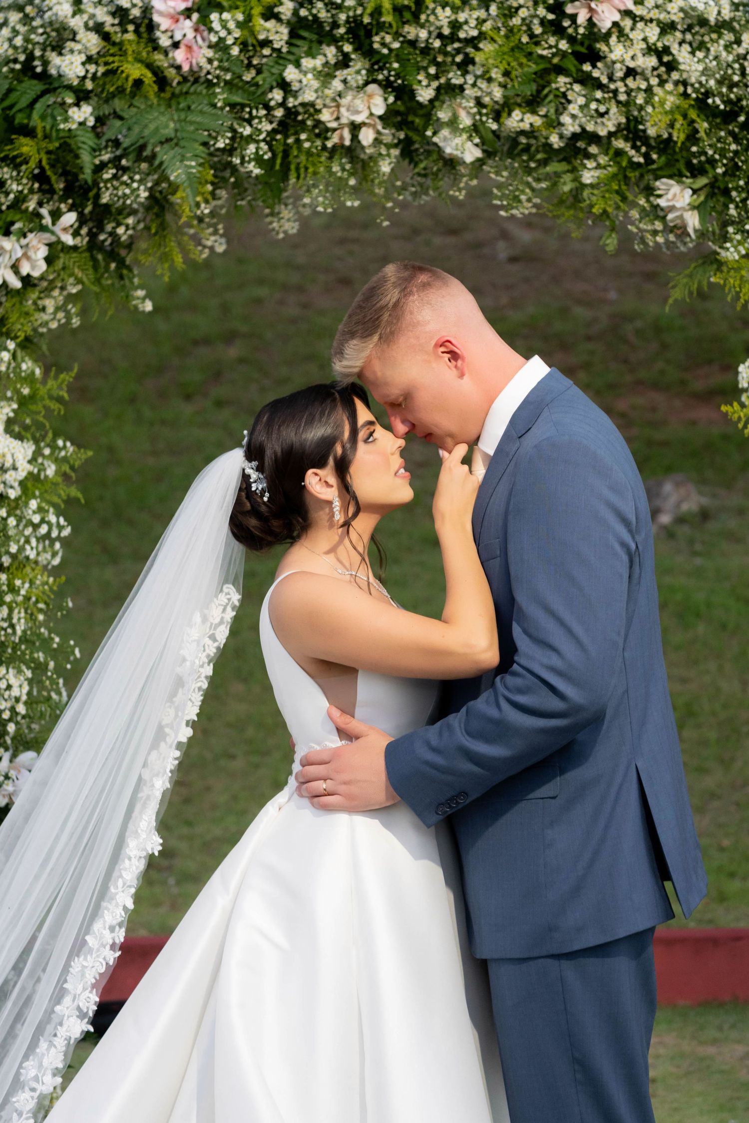 Bride and groom share a romantic embrace under a floral arch on their wedding day outdoors.
