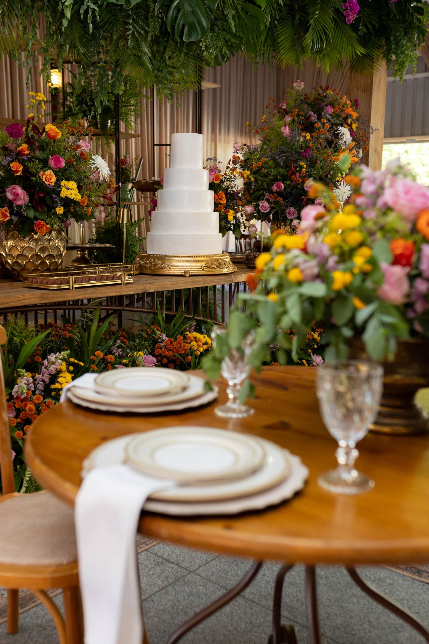 Elegant wedding reception with tiered white cake, colorful floral arrangements, and a round wooden table with fine china place settings.