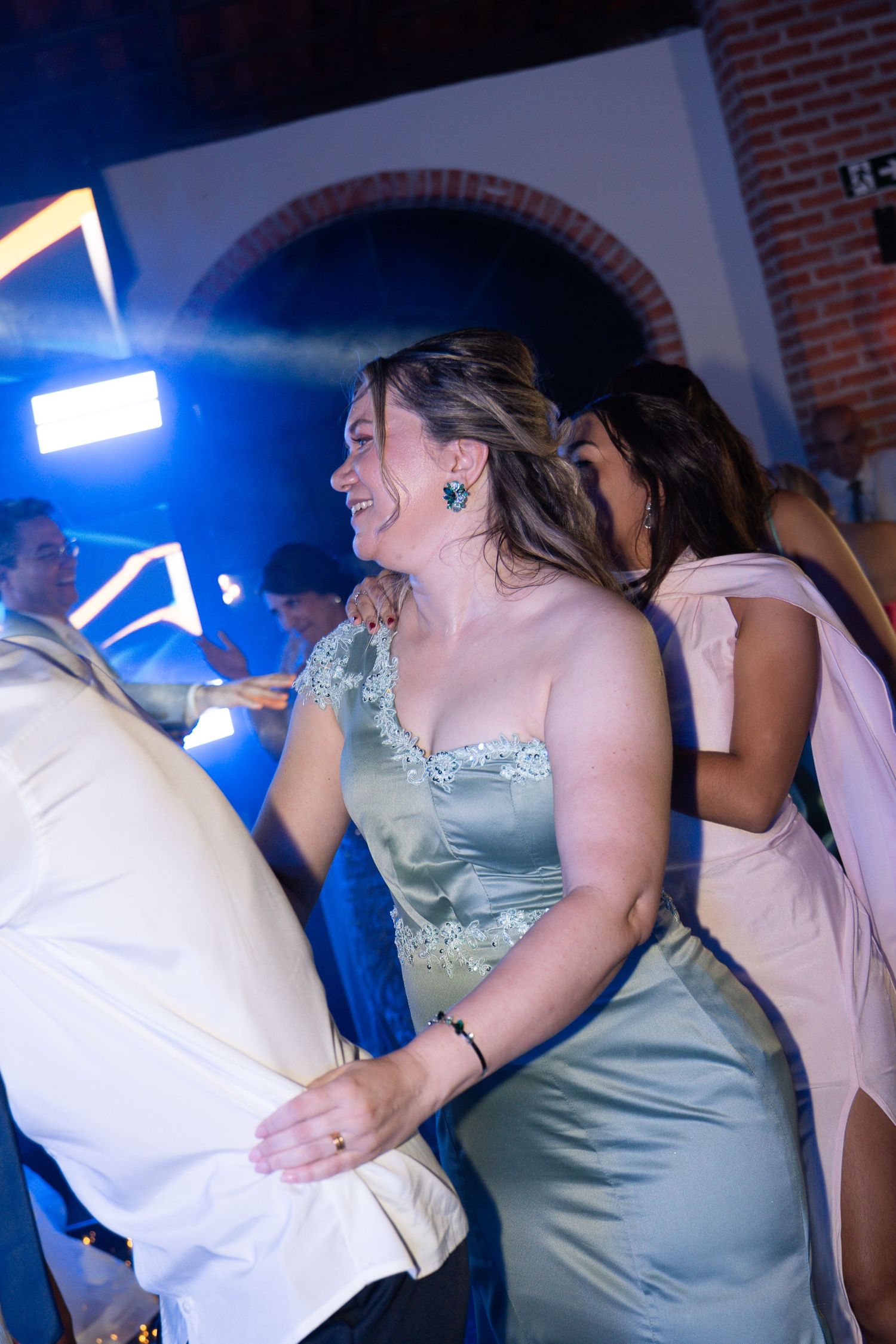 Woman in sage green satin gown dancing joyfully at a formal event with blue lighting.