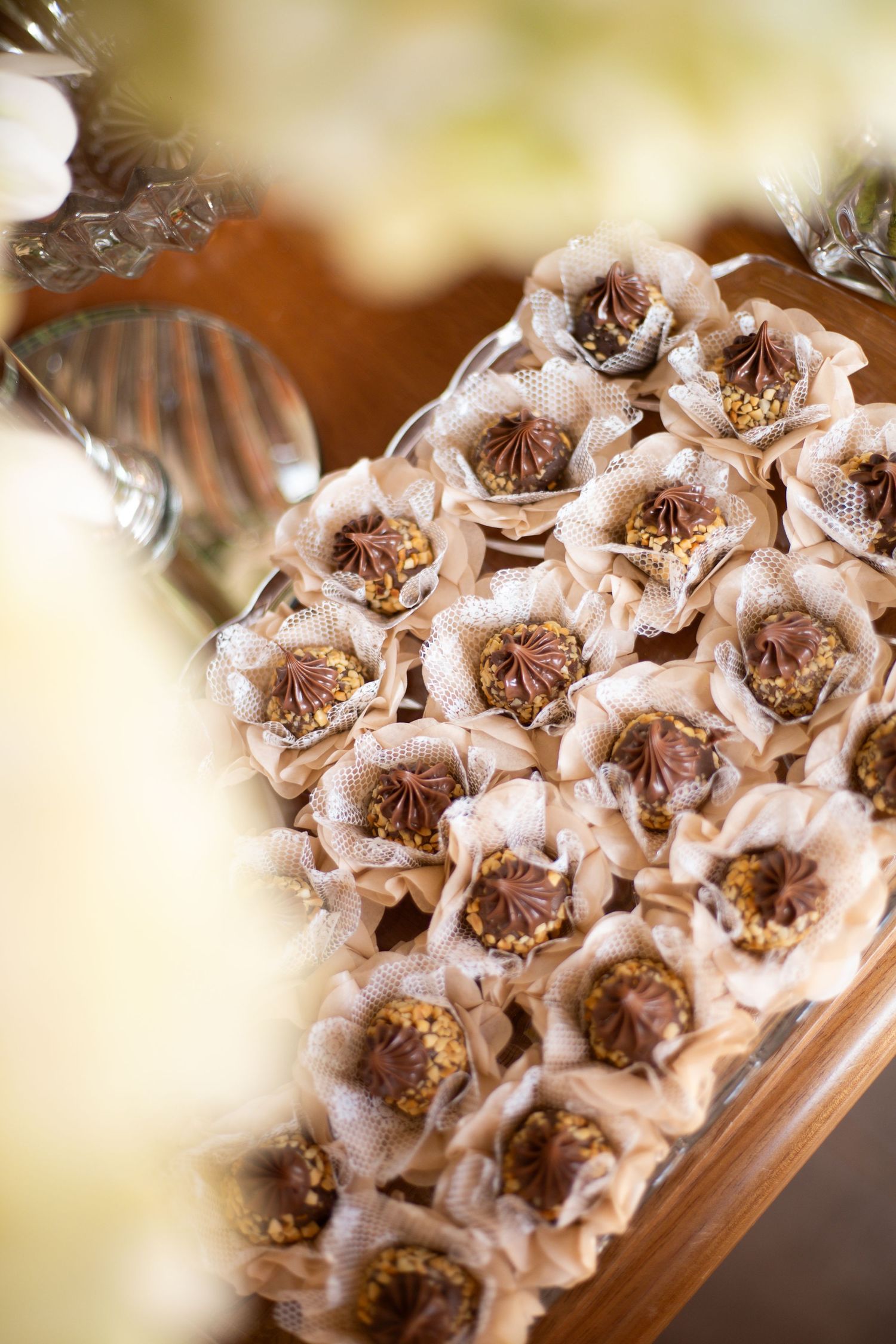 Elegant chocolate Ferrero Rocher candies wrapped in beige lace flower paper cups displayed on a wooden heart-shaped tray.