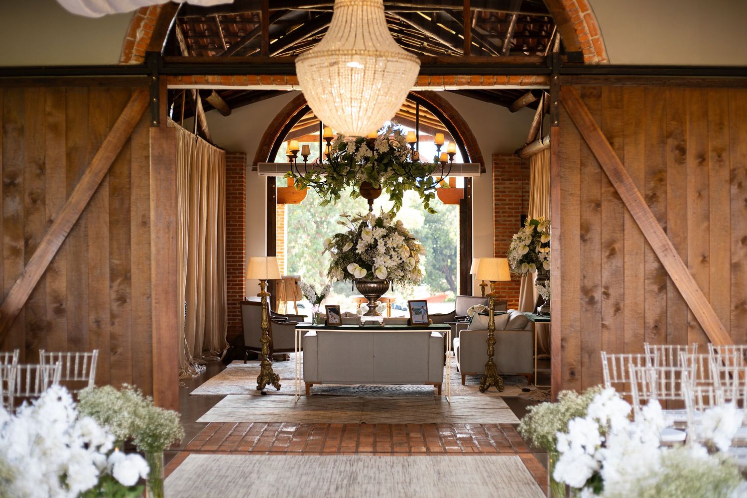 Elegant barn wedding venue with wooden walls, chandelier, white floral arrangements, and a cozy seating area in natural light.