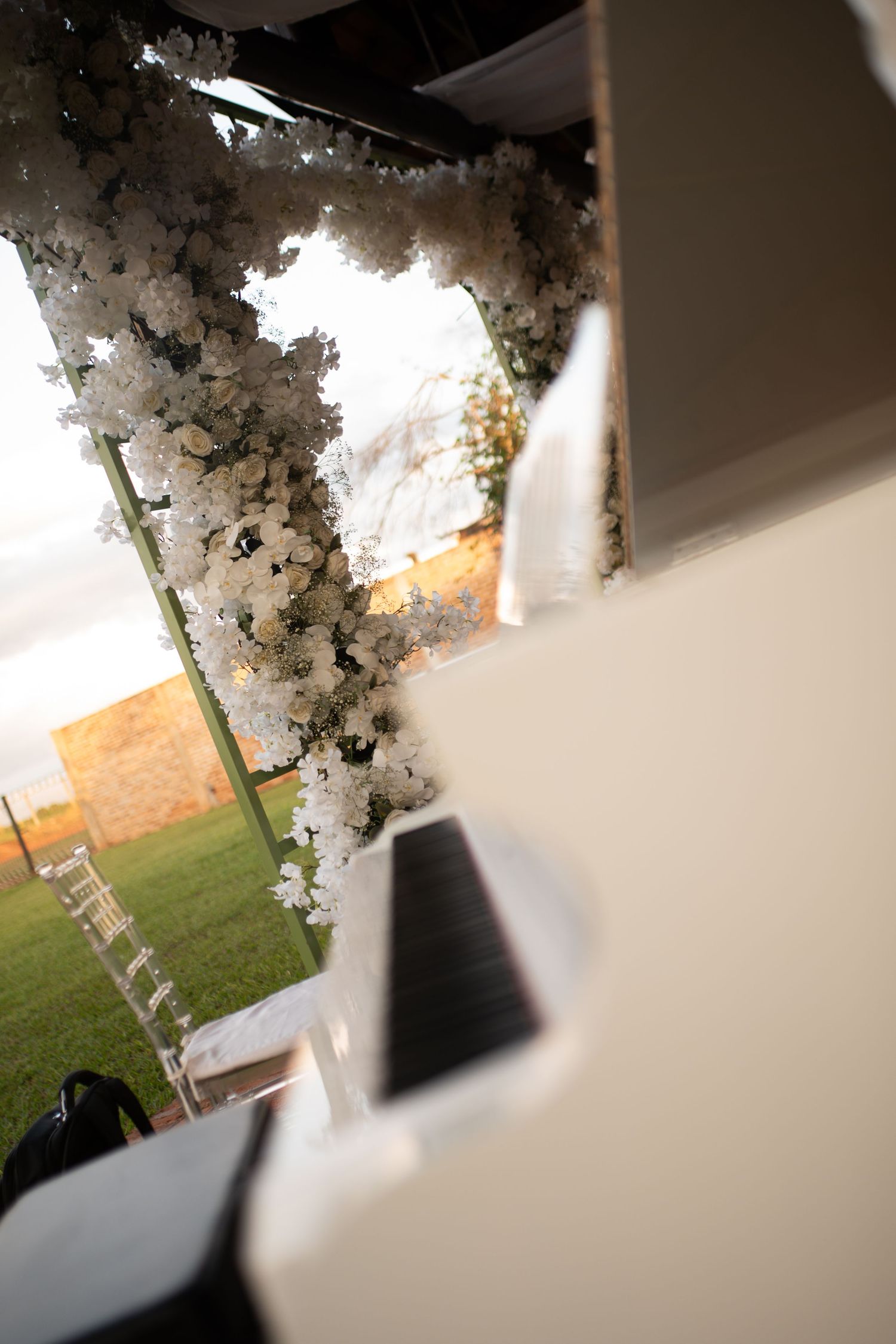 White floral wedding arch with cherry blossoms on green lawn at golden hour, with piano keys in foreground.