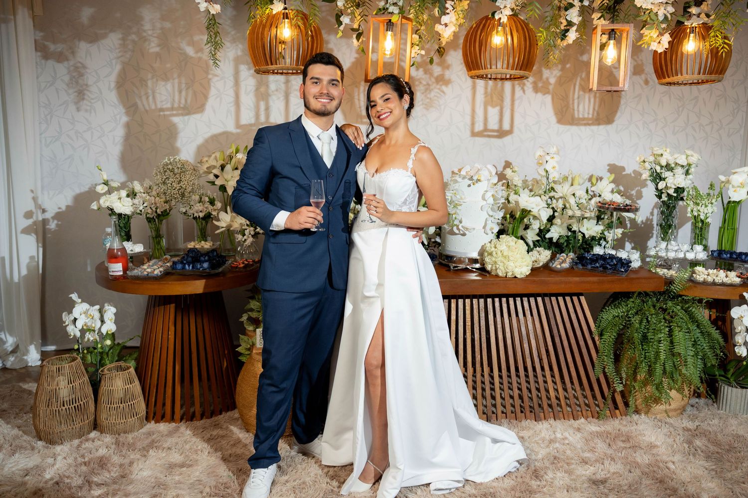 Elegant bride and groom posing together at wedding reception with floral decorations and warm pendant lights.