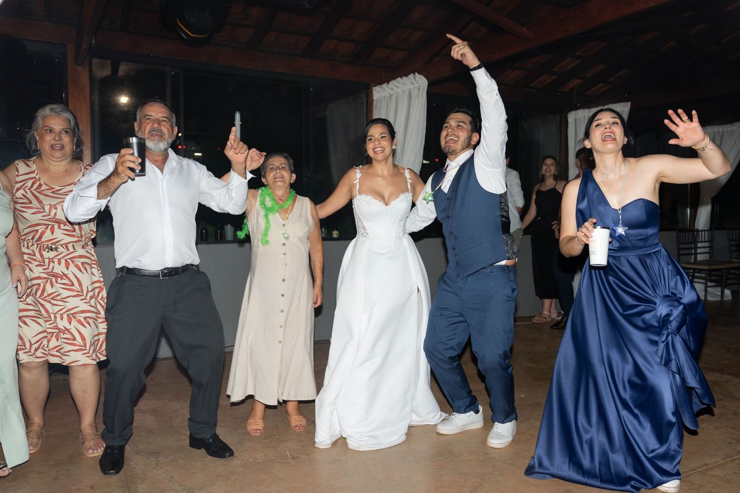 Wedding party guests dancing joyfully at a reception, with bride in white gown and guests in formal attire.
