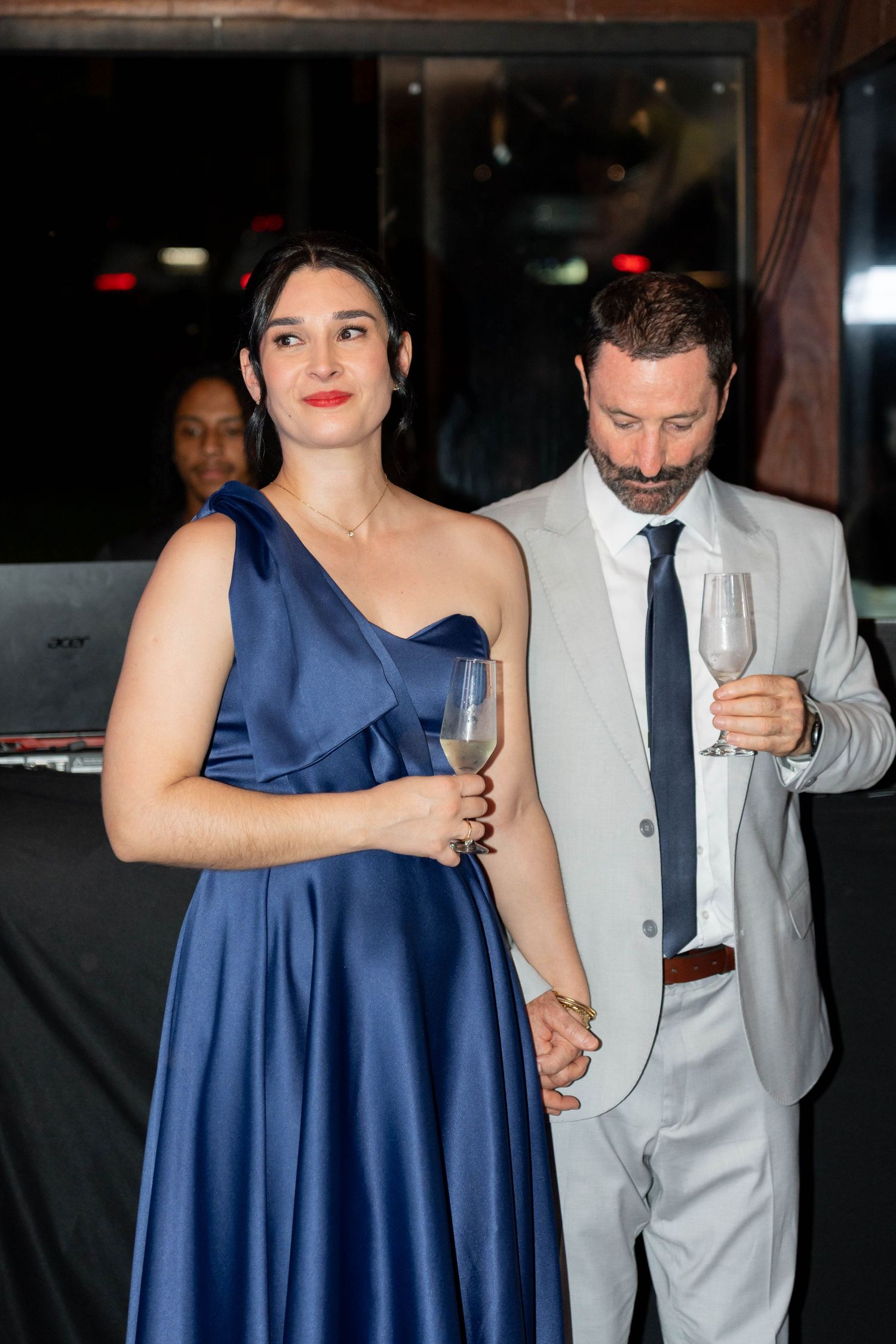 Elegant couple in formal attire holding champagne glasses at a gala event, woman in blue gown, man in gray suit.