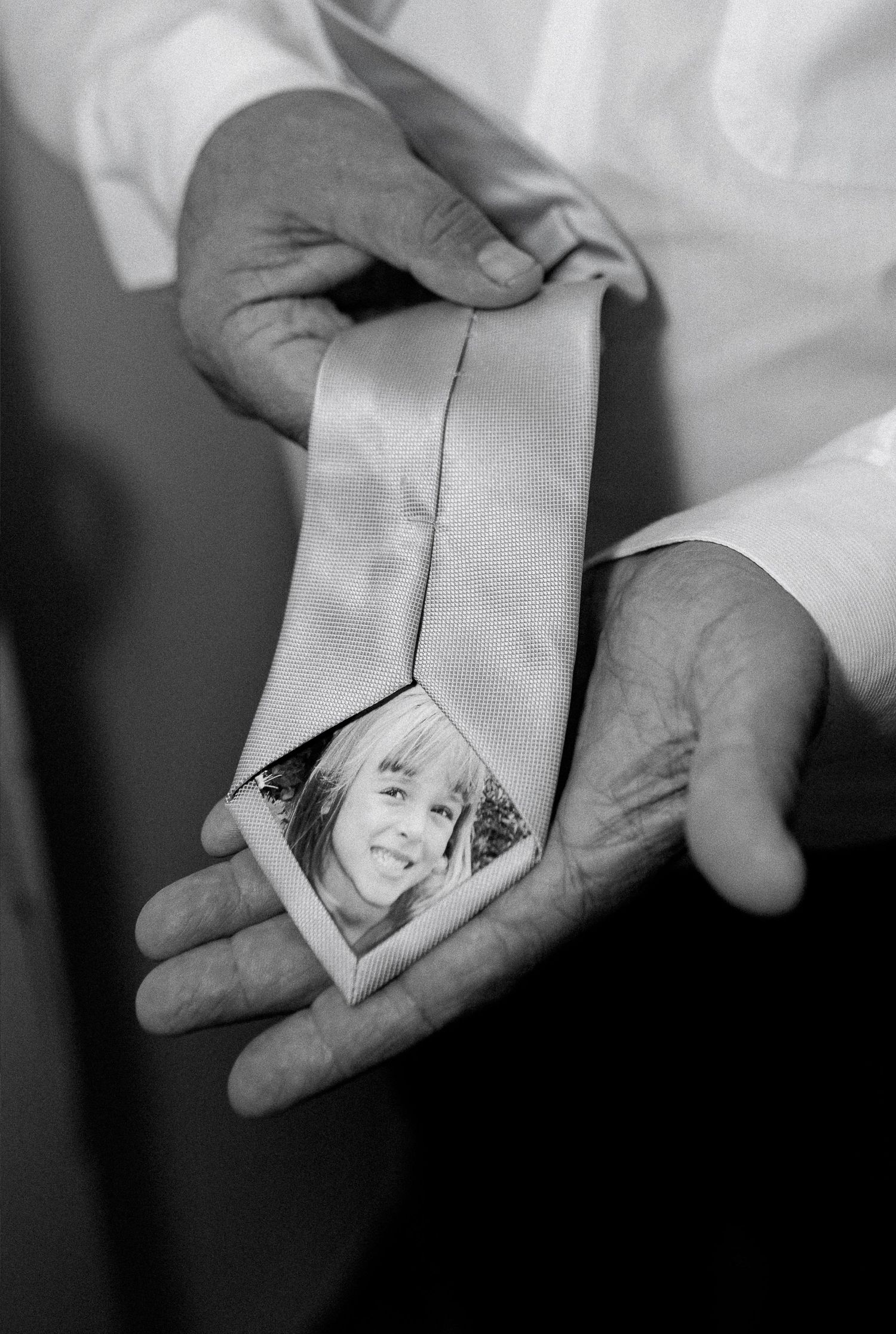 Groom holding a tie with a photo of the bride inside in a sentimental wedding detail.