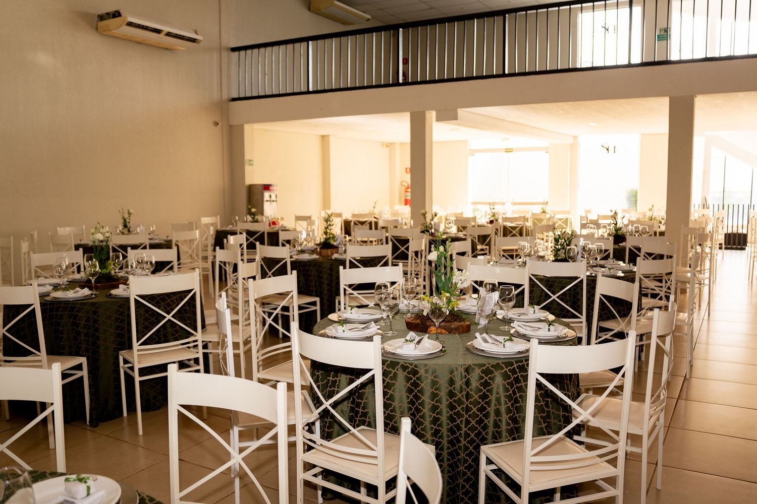 Elegant banquet hall with white cross-back chairs, round tables with dark green linens, and floral centerpieces for a formal event.