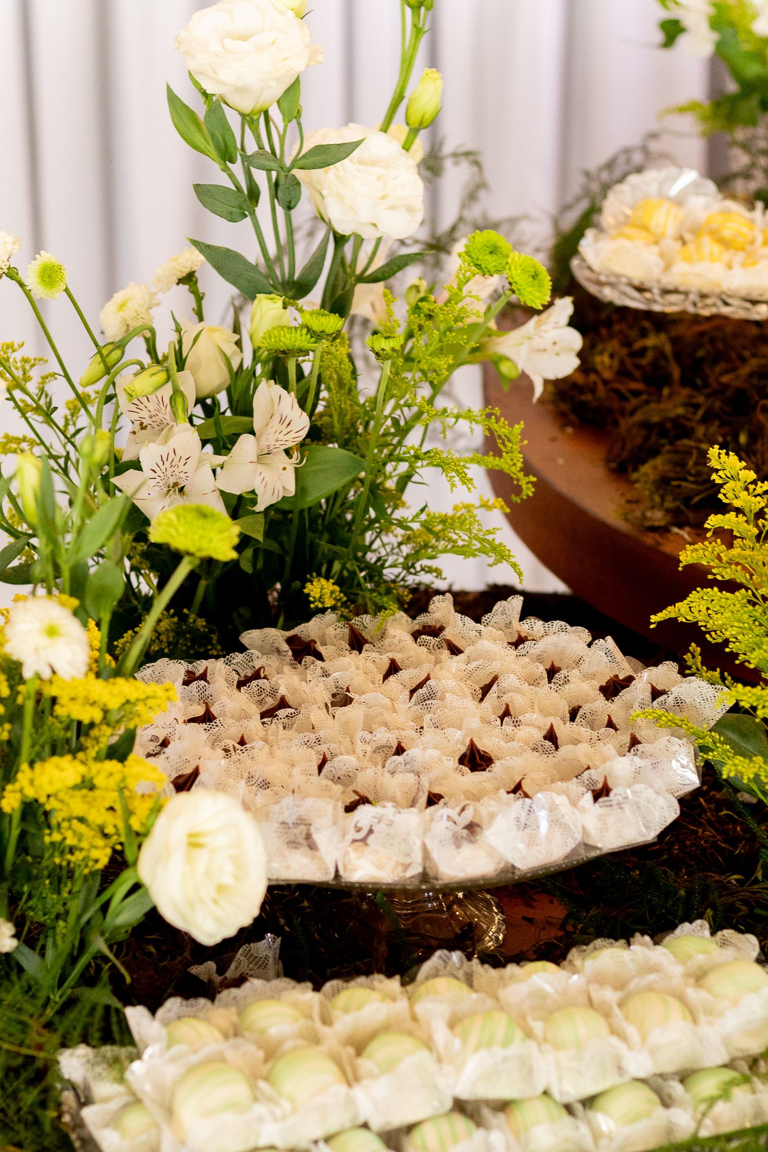 Elegant dessert table with white and yellow floral arrangements, decorated sweets, and rustic wooden accents for a special event.