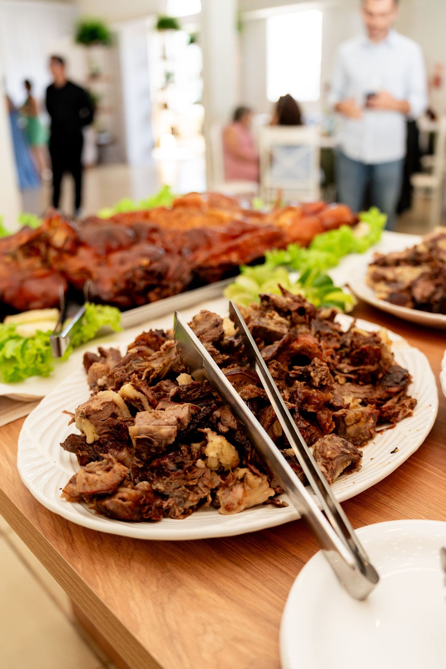 A buffet spread featuring a plate of carved roasted meat with tongs, garnished with lettuce, at a catered event.