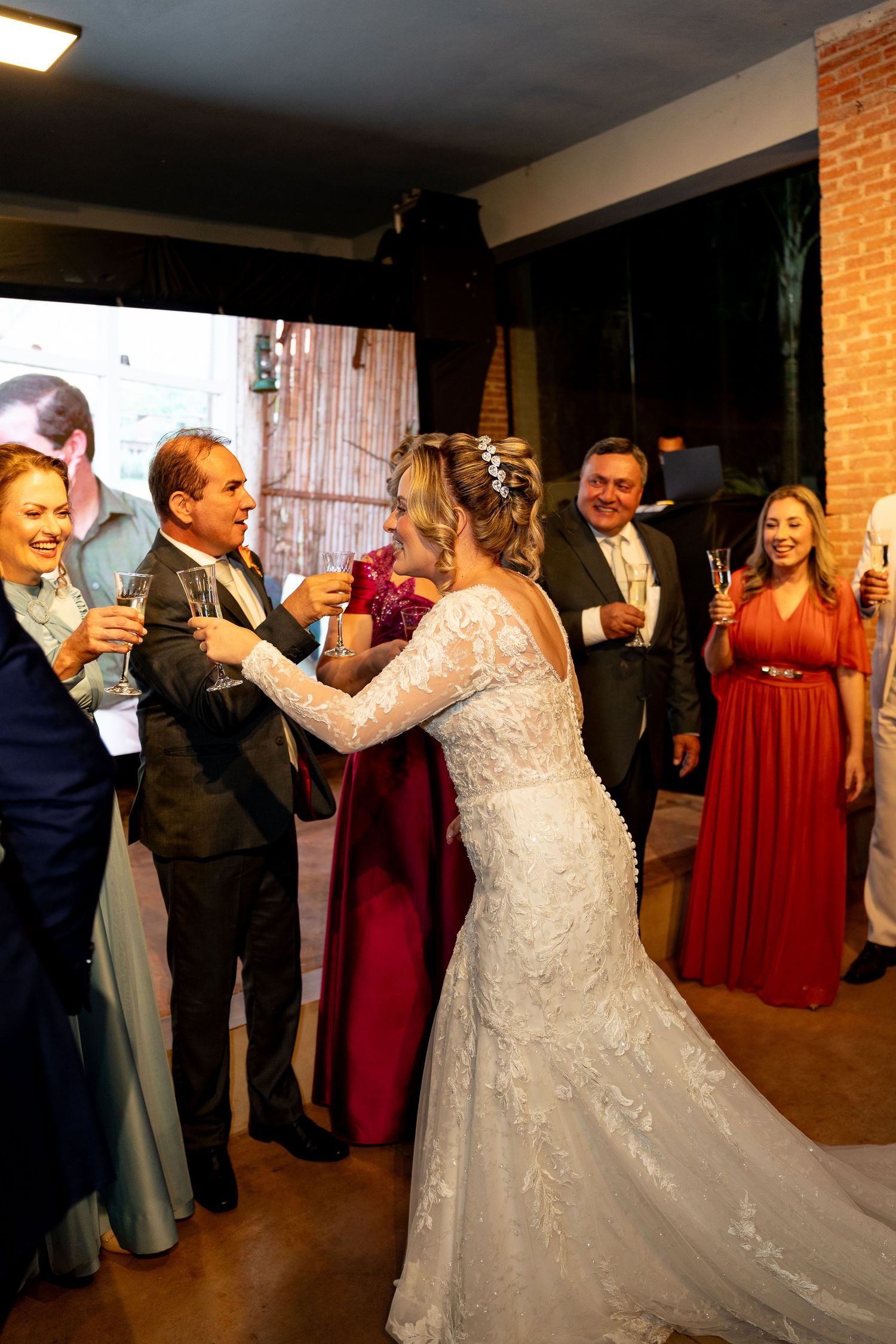Bride in lace gown toasts with groom and guests in formal attire at elegant wedding reception.