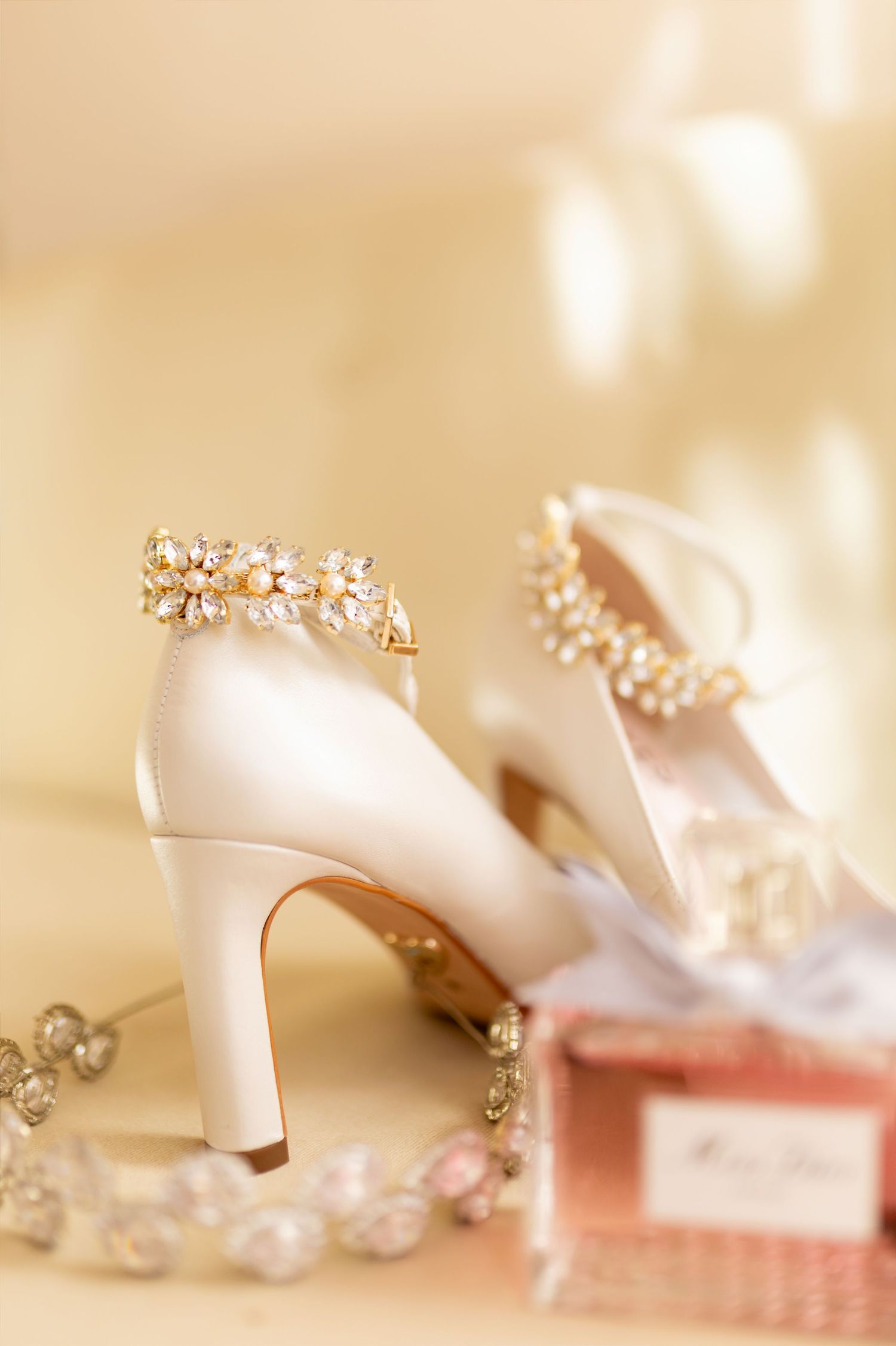 Elegant ivory bridal heels adorned with gold crystal embellishments beside a Miss Dior perfume box.