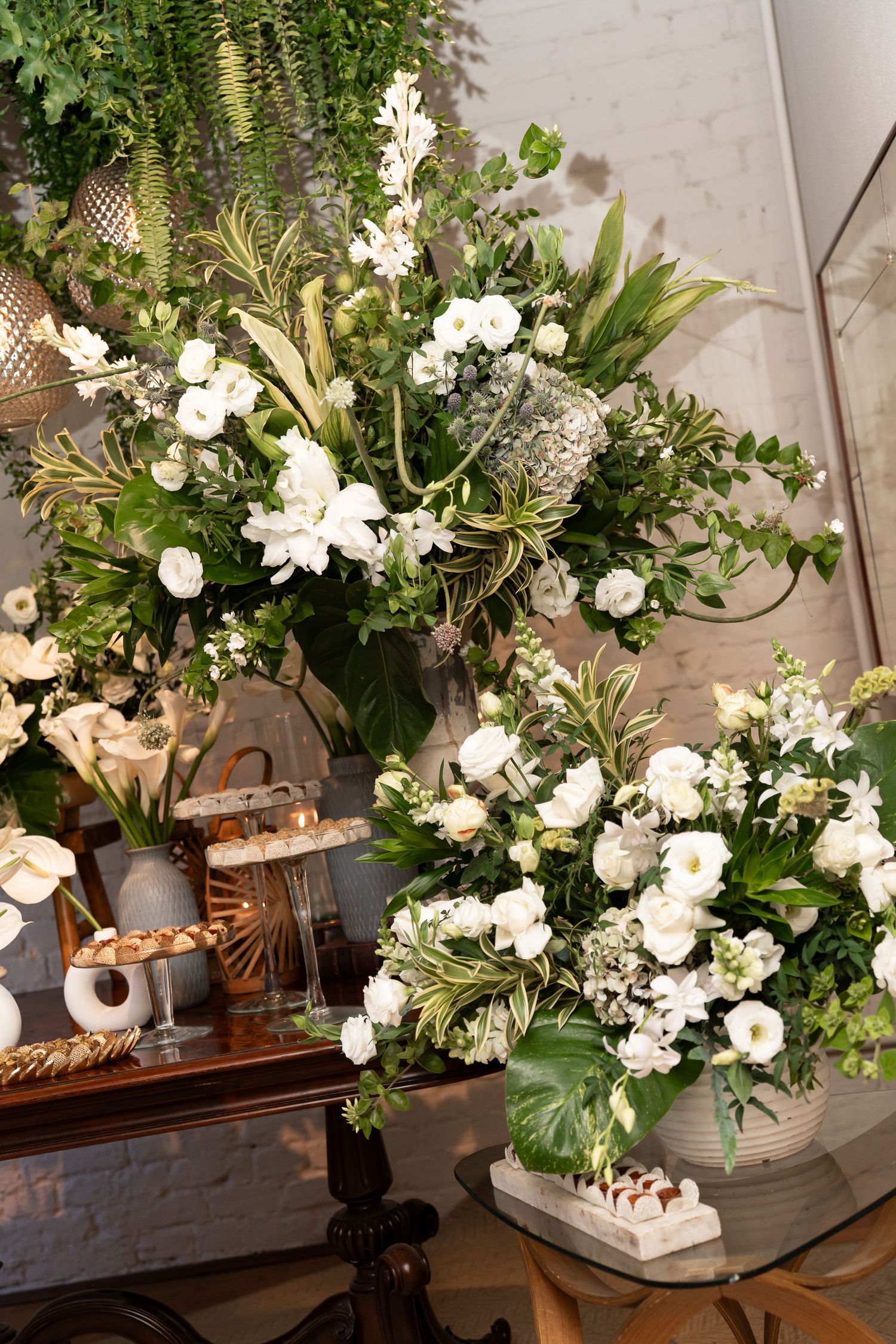Lush white floral arrangements with greenery displayed on elegant stands at a wedding or event venue.