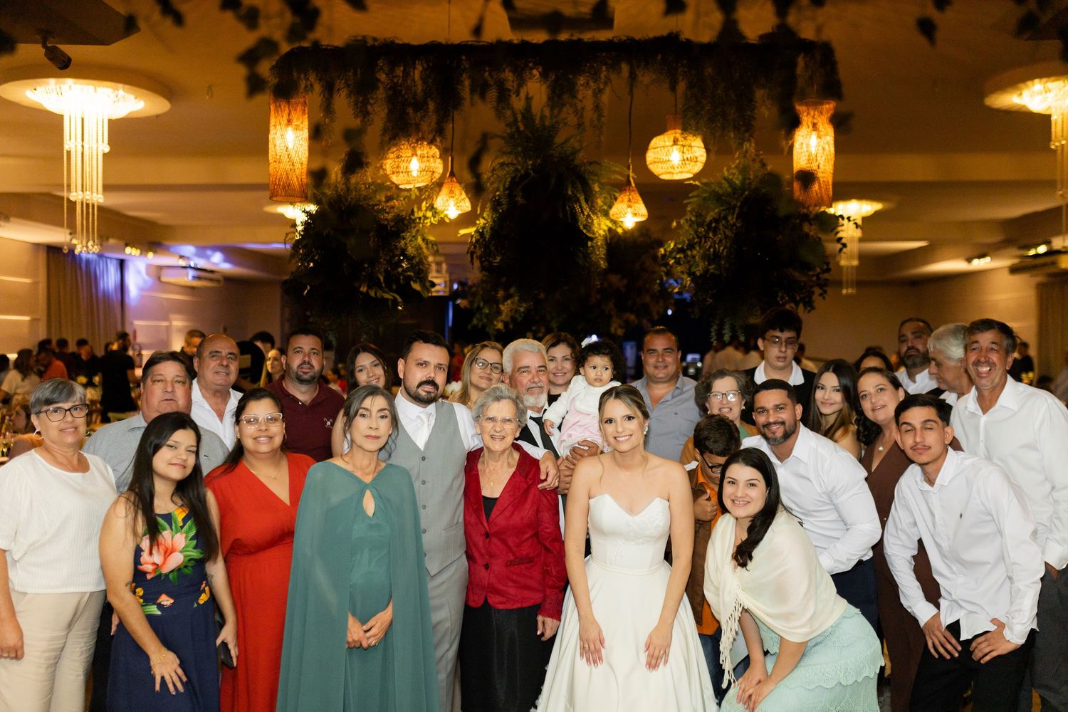 A large group of wedding guests poses with the bride and groom in an elegantly decorated reception venue.