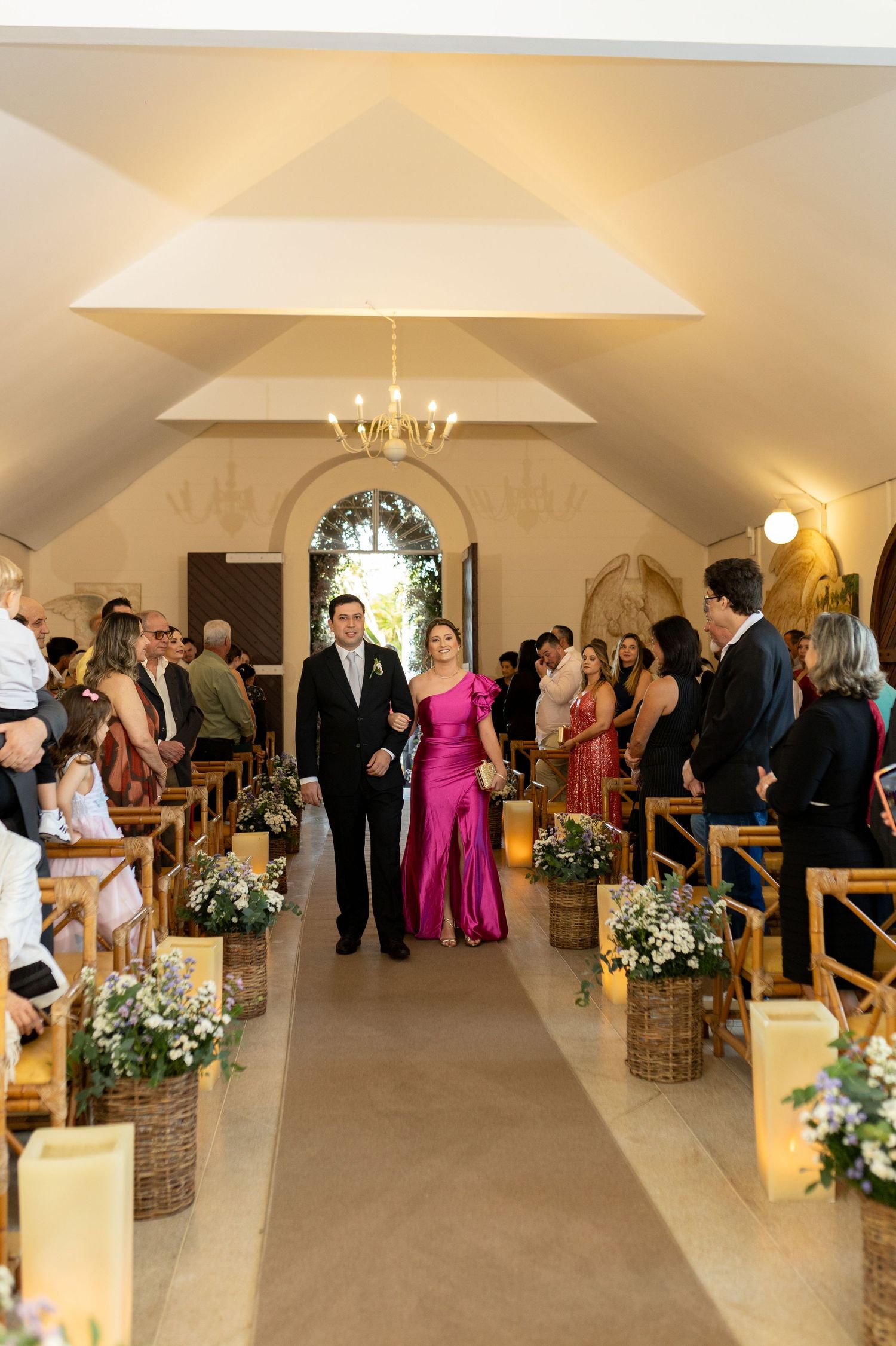 Elegant wedding processional in a chapel with floral arrangements lining the aisle as a couple walks toward the altar.