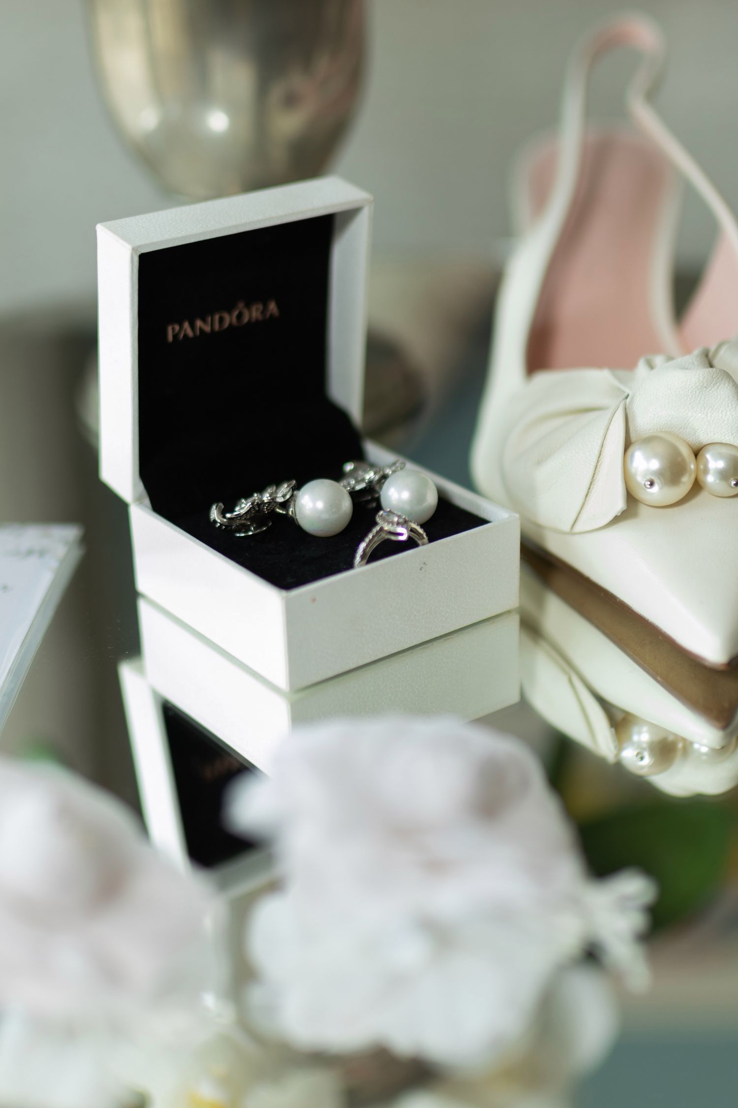 Pandora jewelry box with pearl earrings and ring beside white bow heels and pearls for a wedding.