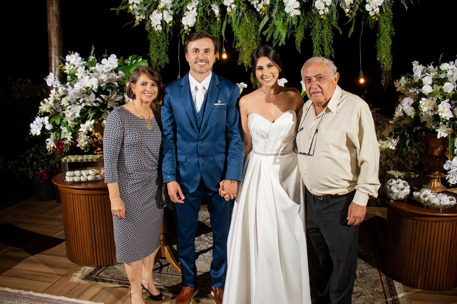 Bride and groom pose with family members at an elegant outdoor wedding reception with floral decorations.