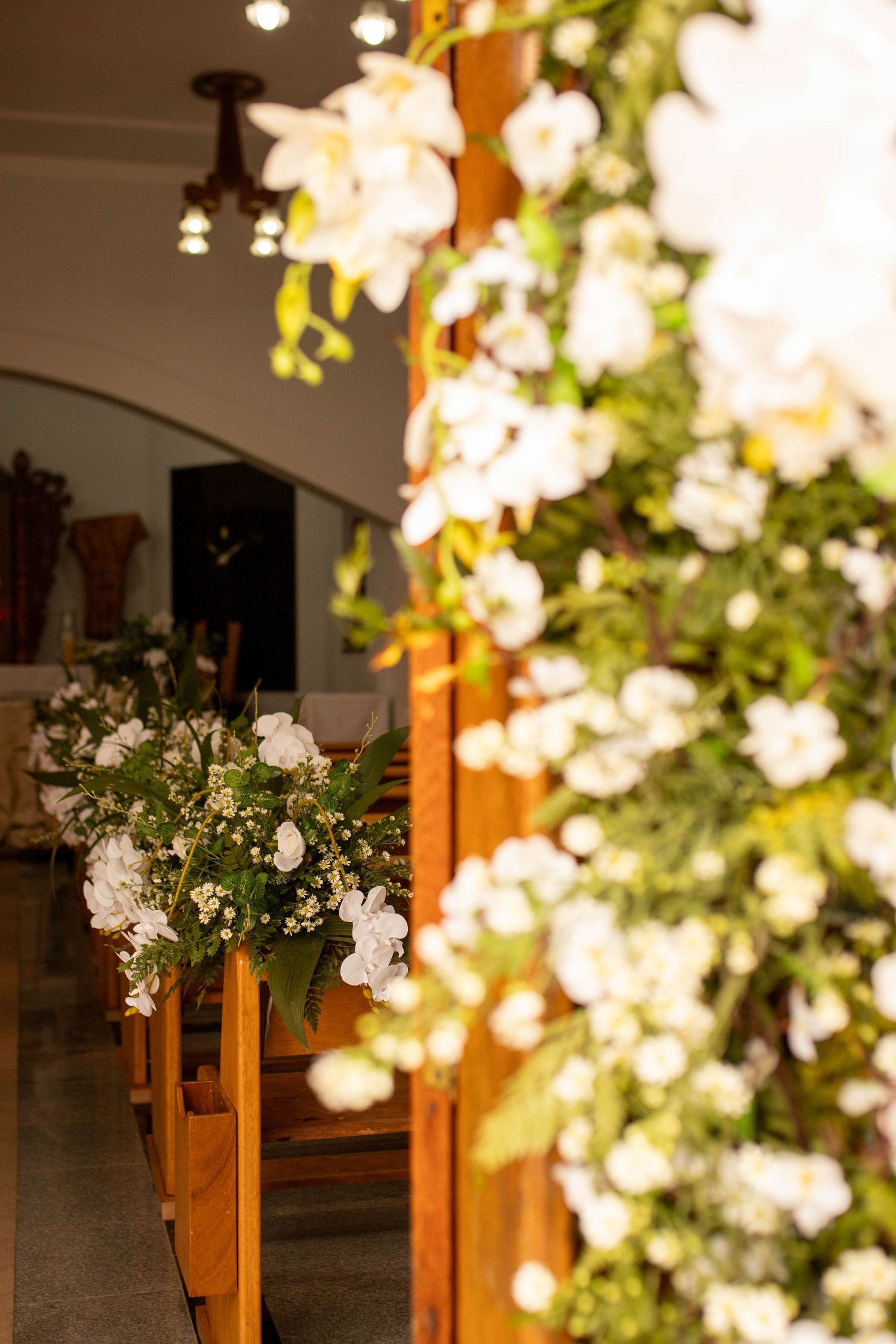Church aisle decorated with white orchids and greenery on wooden pews for an elegant wedding ceremony.