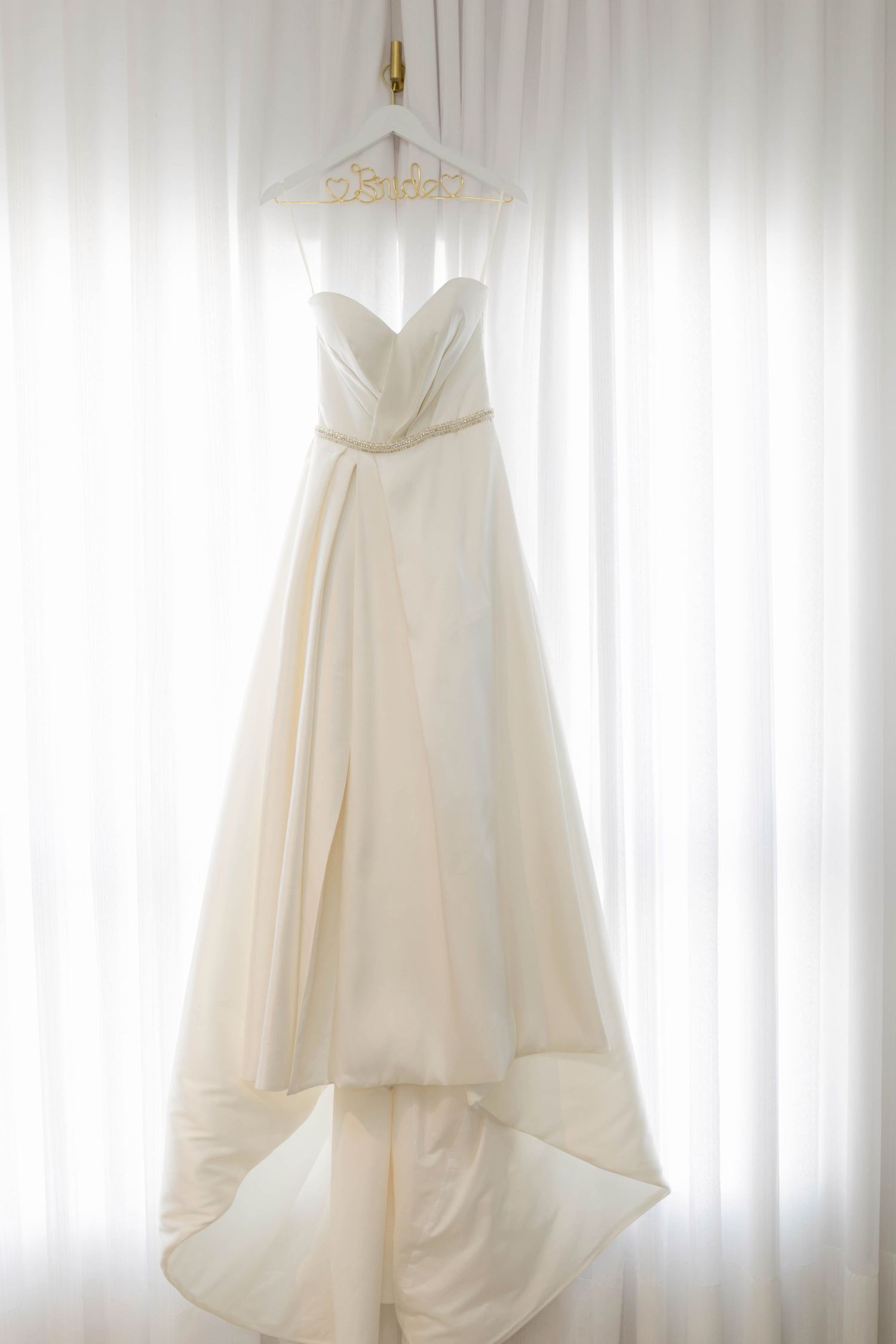 Elegant strapless ivory wedding gown with sweetheart neckline and high-low skirt hanging on a decorative hanger.