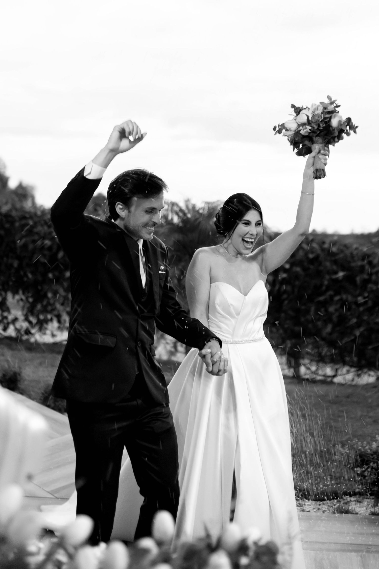 Black and white photo of joyful newlyweds celebrating after wedding ceremony, bride holding bouquet aloft.