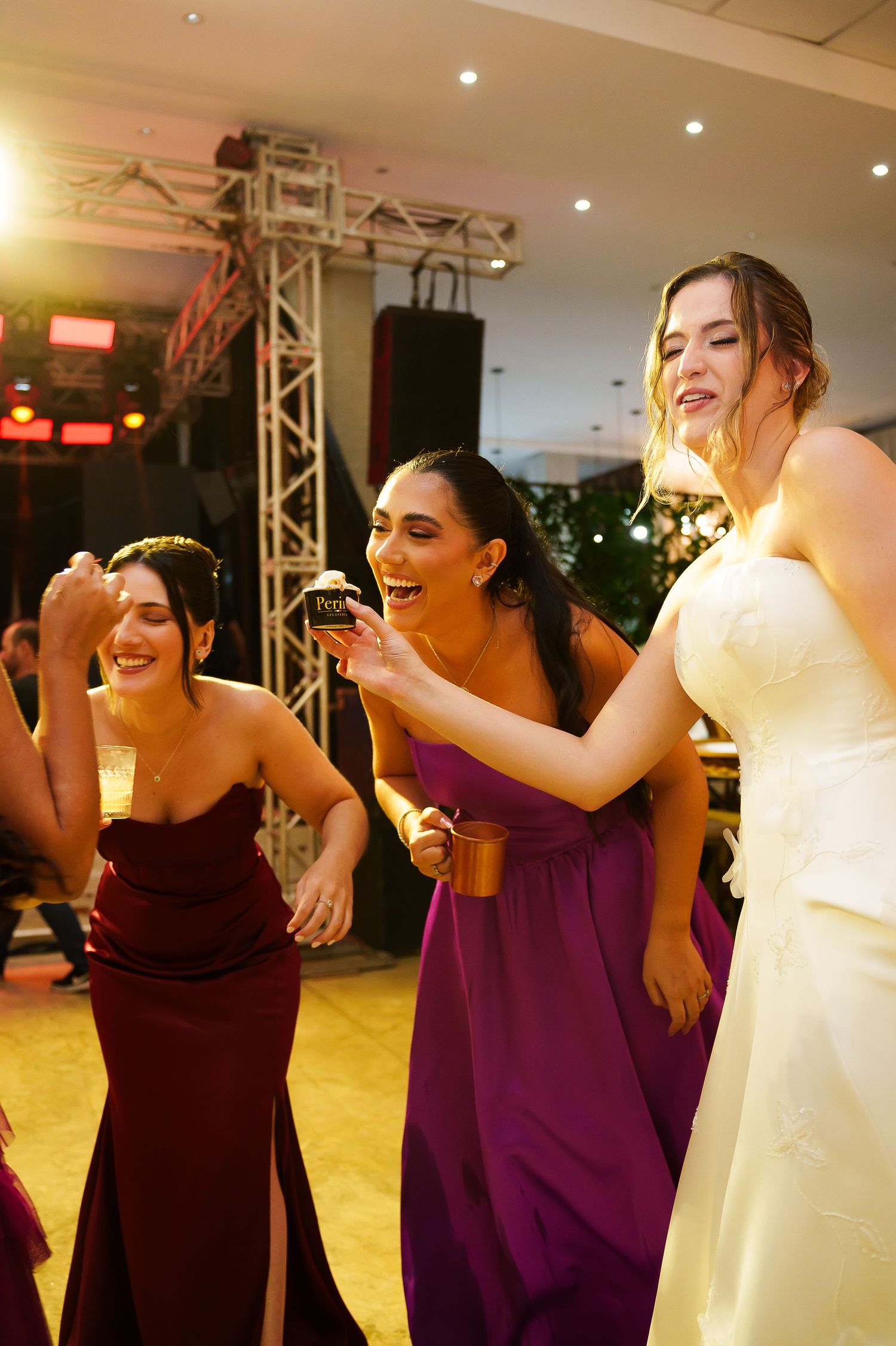 Bride and bridesmaids in purple gowns laughing and dancing joyfully at a wedding reception.