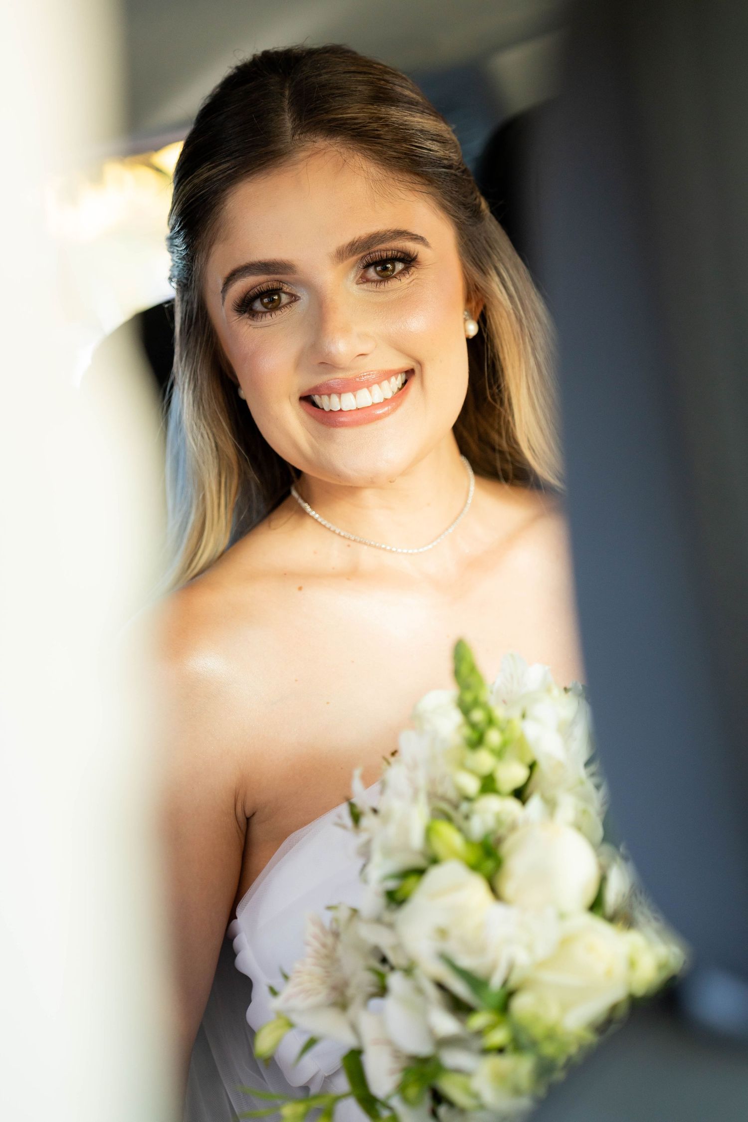 Smiling bride in strapless gown holding white floral bouquet with roses and greenery on her wedding day.