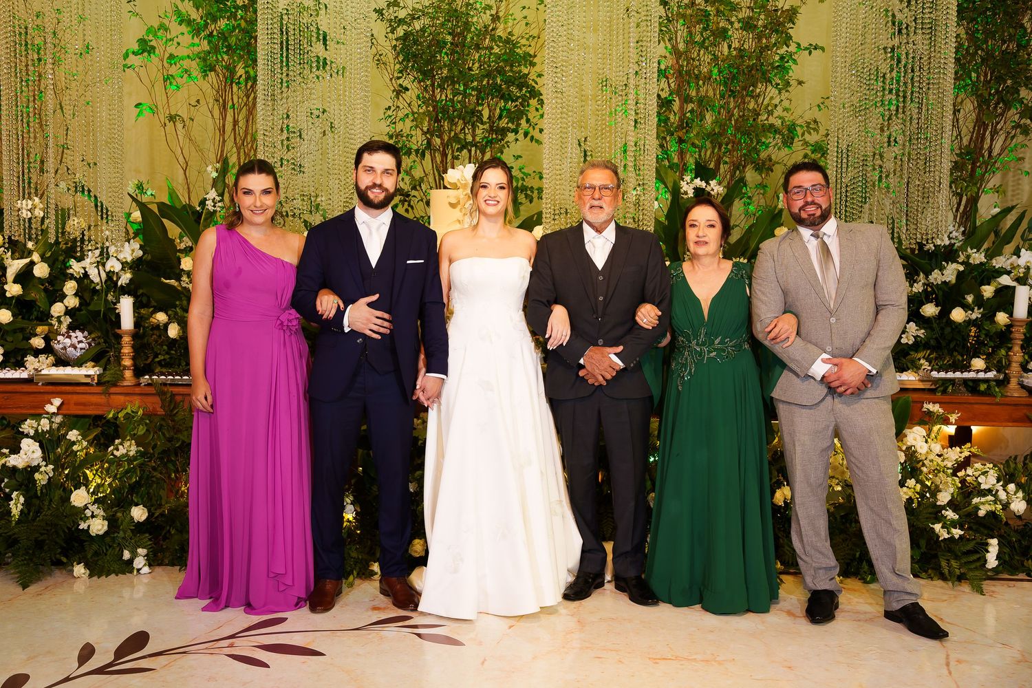 Wedding party posing together, bride in white gown with family in formal attire at elegant floral venue.