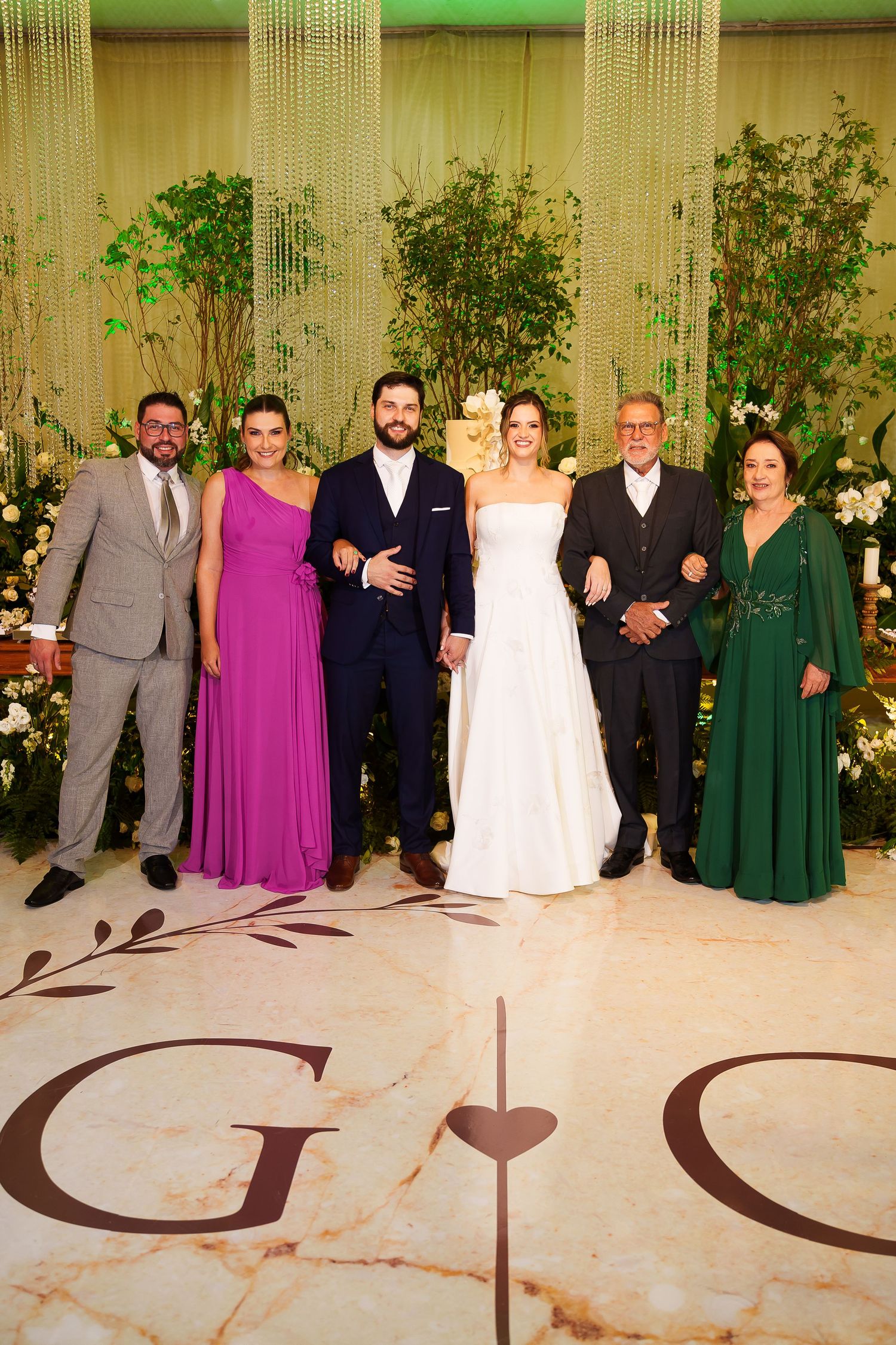 A wedding party of six poses on a marble dance floor with monogram, featuring a bride in white and guests in formal attire.