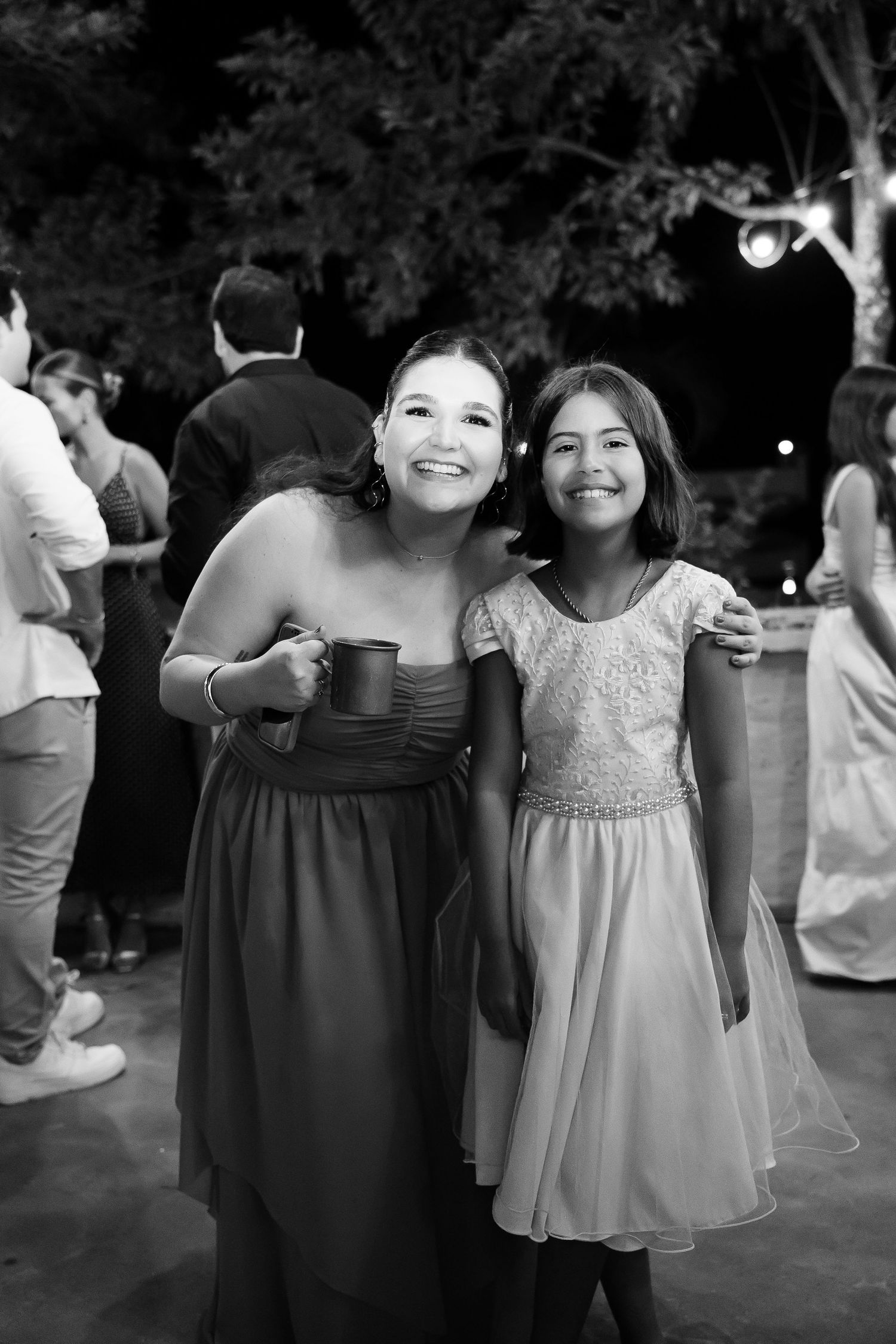 Two smiling females pose together at an outdoor evening wedding reception in black and white photo.