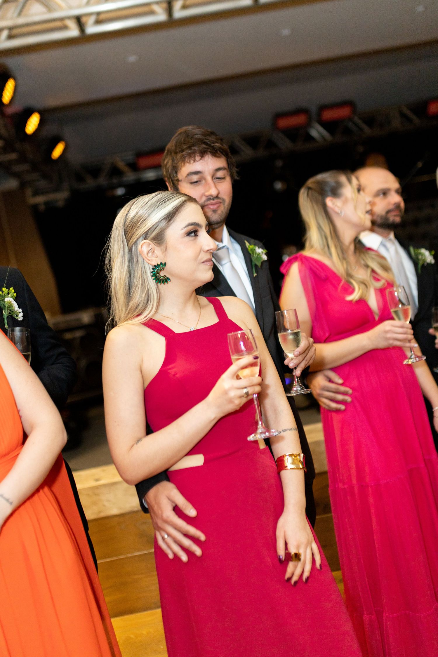 Guests in red and orange formal dresses holding champagne glasses at an elegant indoor wedding reception.