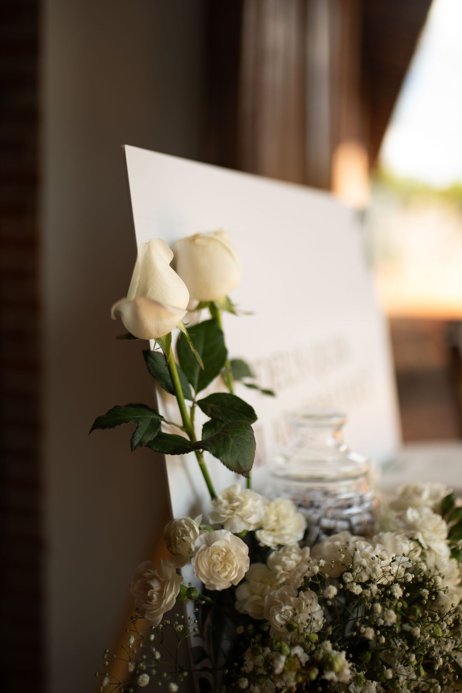 White roses and delicate floral arrangement beside a wedding sign, perfect for elegant event decor.