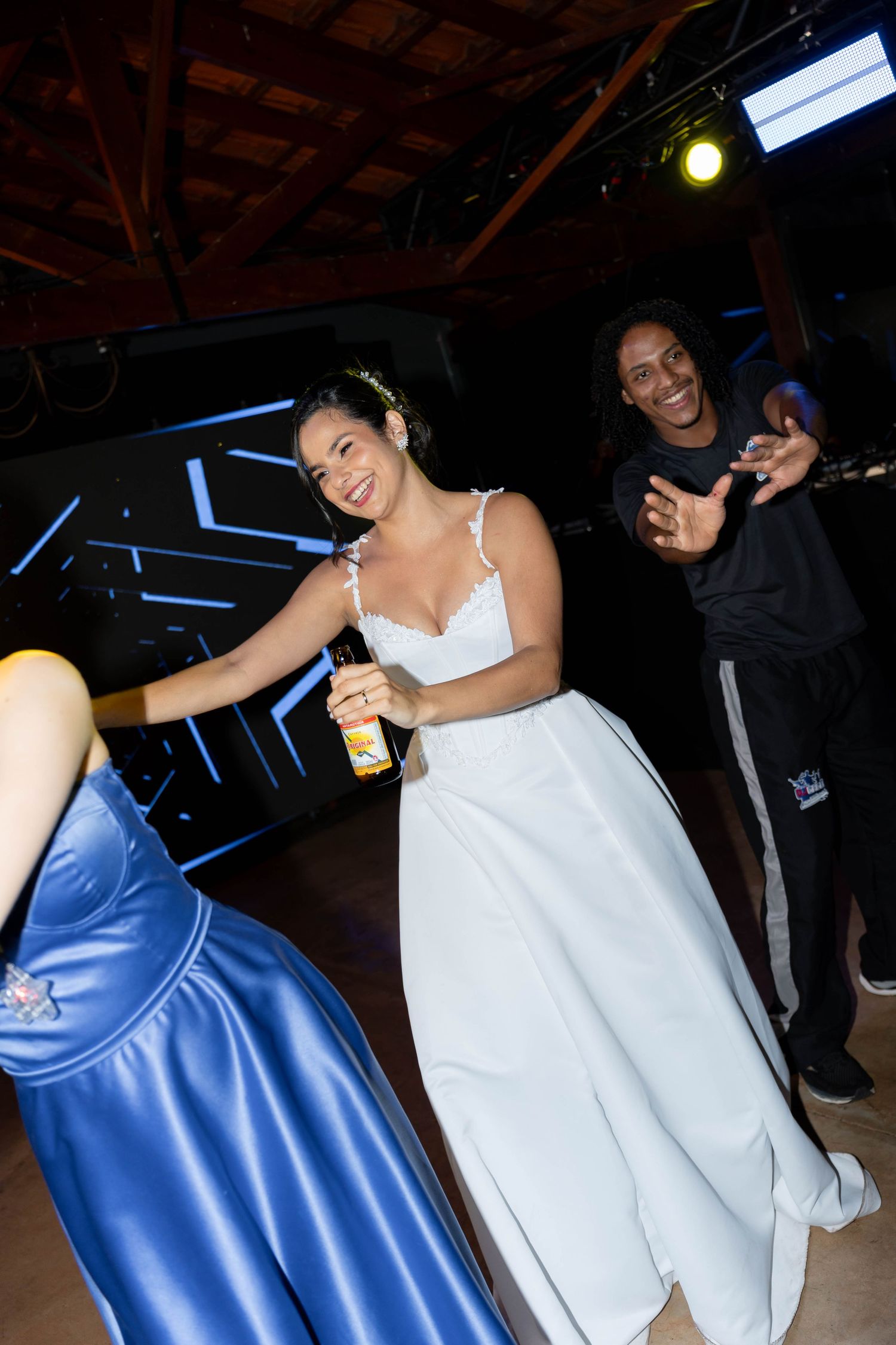 Bride in white gown holding a drink laughs with a guest on the dance floor at a vibrant evening reception.