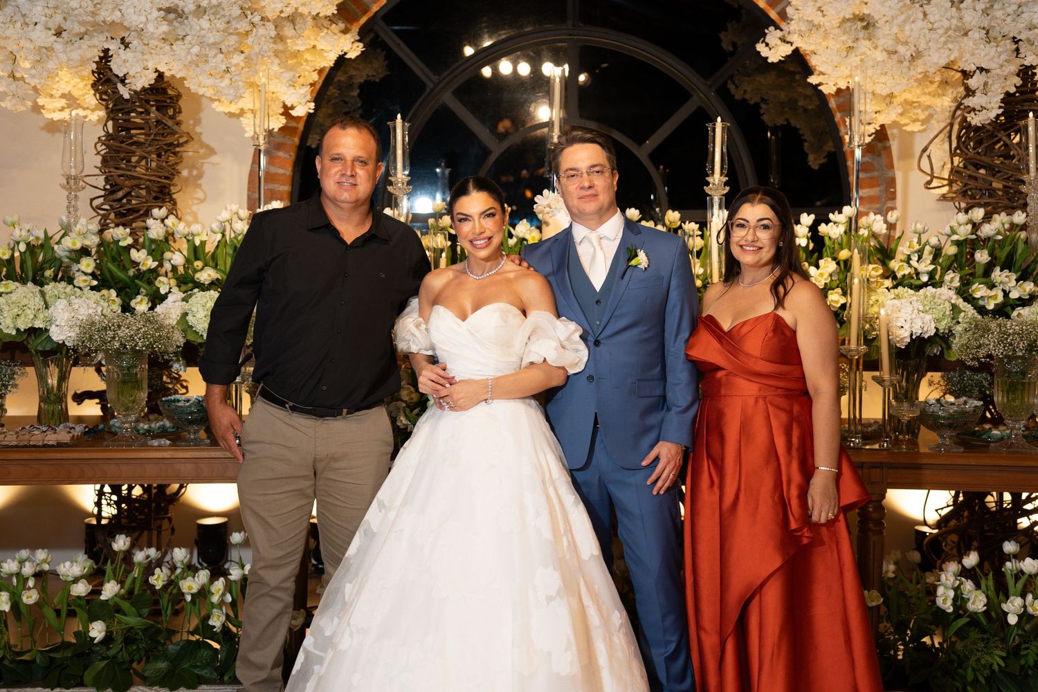 Bride and groom pose with two guests at elegant floral wedding reception with white orchid decorations.