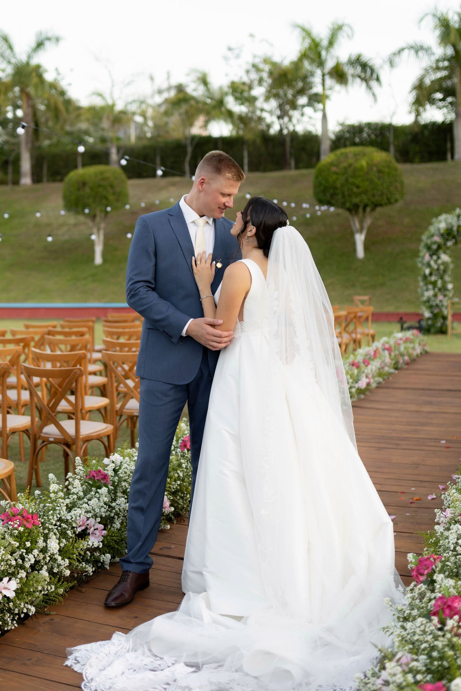 Bride and groom share a romantic moment at outdoor wedding ceremony, surrounded by floral arrangements and wooden chairs.