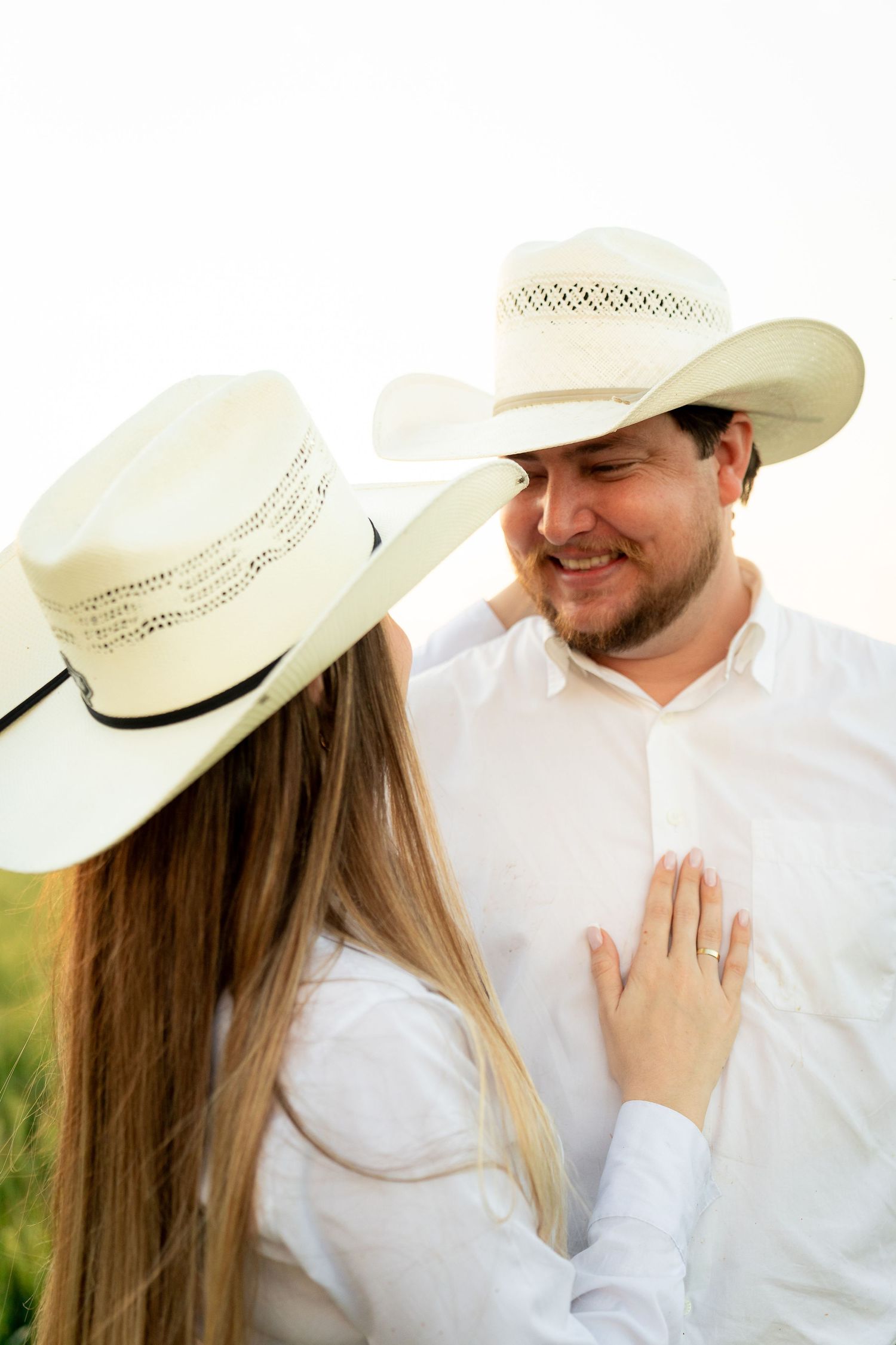 Couple in matching white cowboy hats sharing a romantic moment outdoors, woman placing hand on man's chest.
