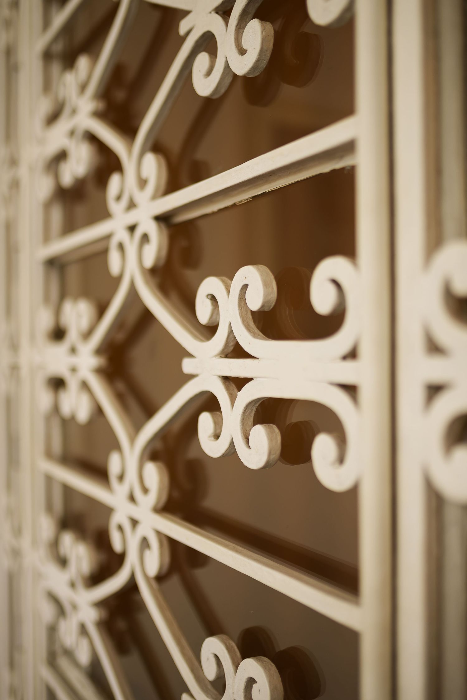 Close-up of ornate white wrought iron window grill with decorative scrollwork and floral patterns on a building facade.