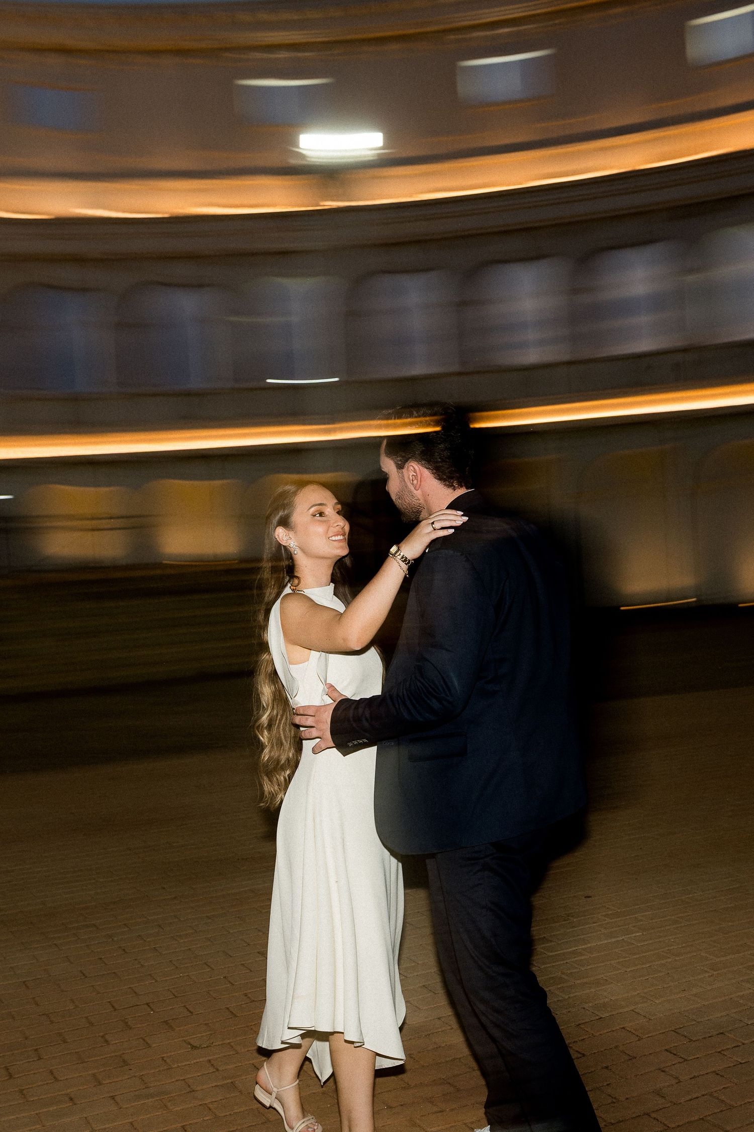 Couple shares a romantic first dance in elegant venue, bride in white dress smiling at groom in dark suit.