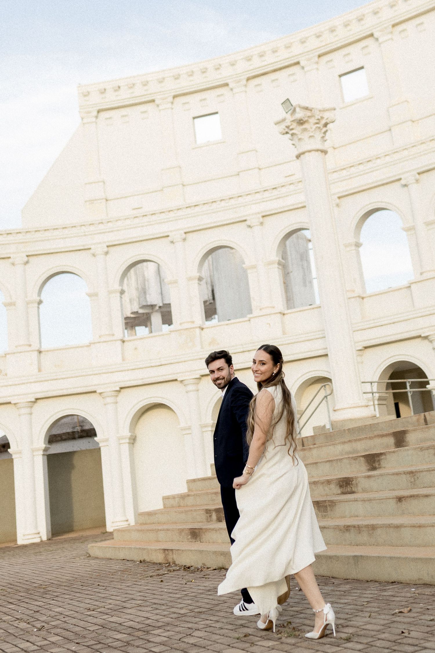 Couple in wedding attire walking hand in hand in front of the Colosseum in Rome, Italy.