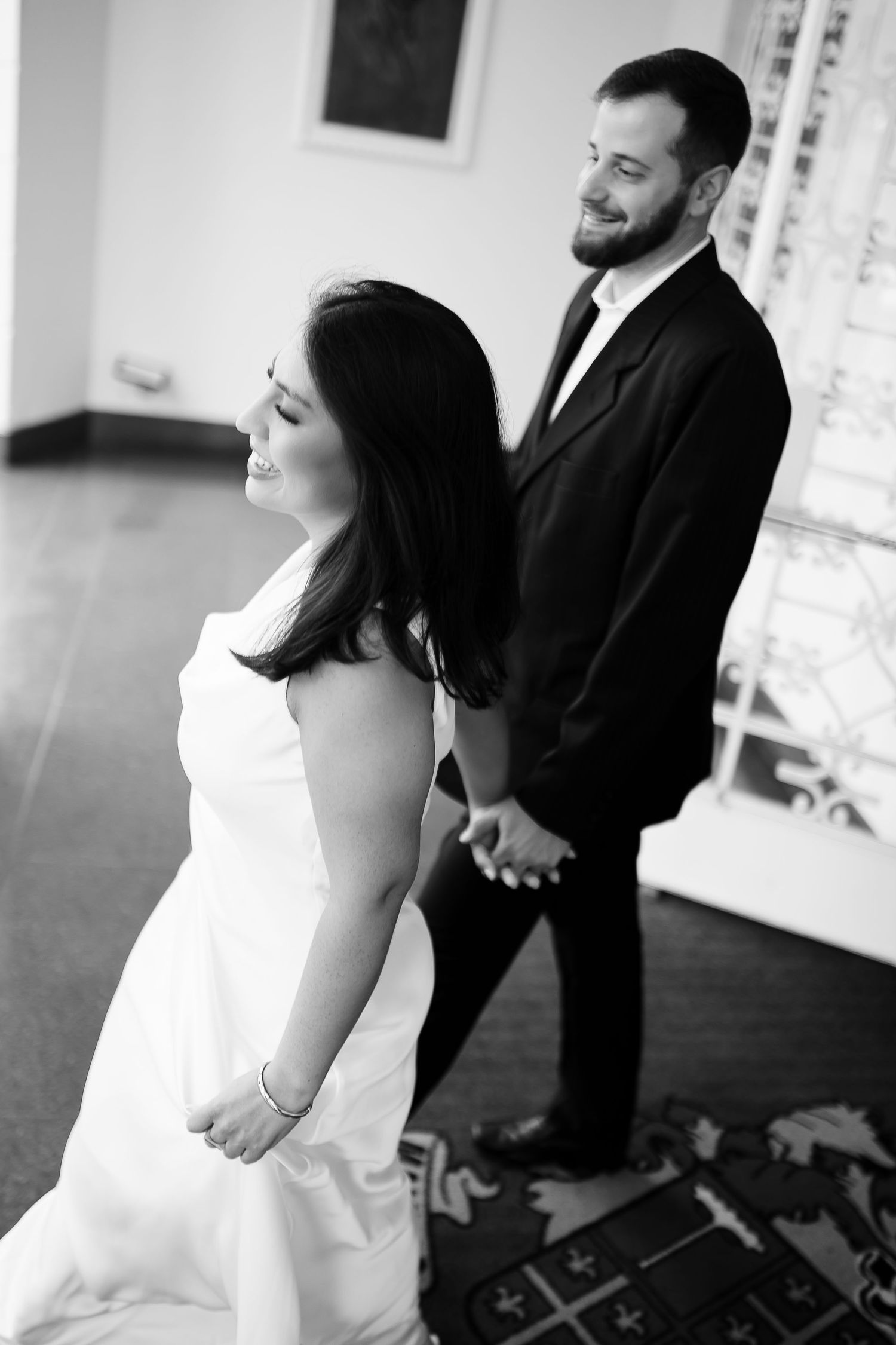 Black and white photo of a bride in white gown and groom in dark suit holding hands at their wedding.