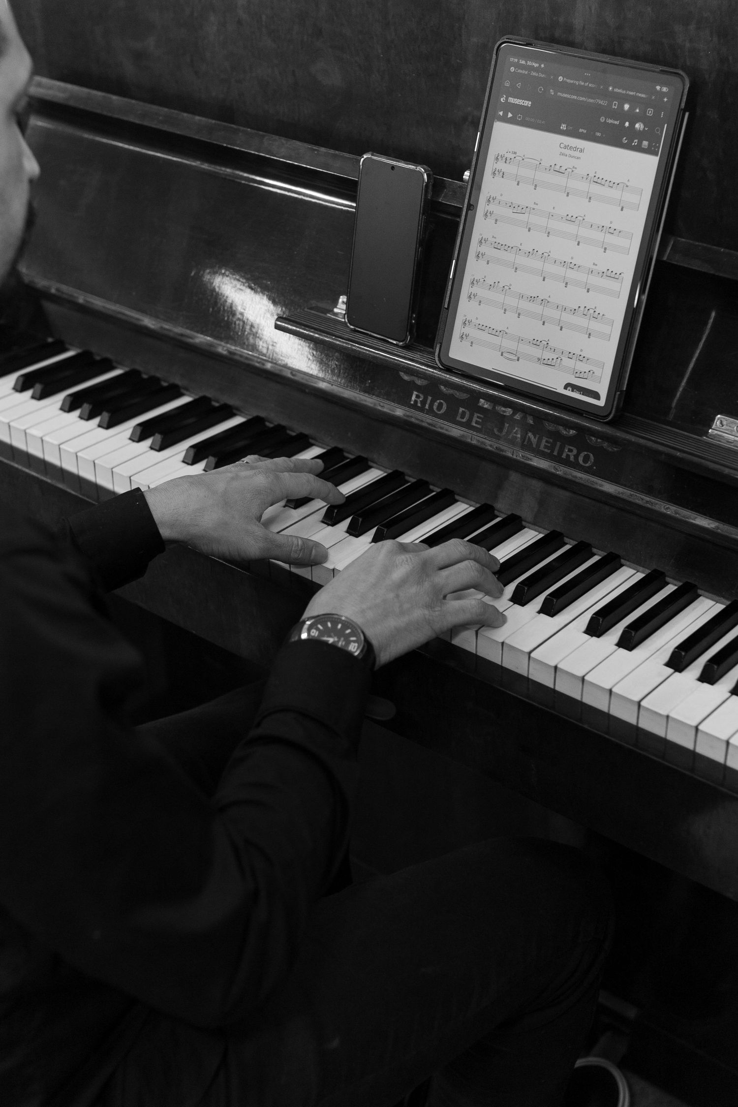 Black and white overhead view of a pianist playing an upright Rio de Janeiro piano with sheet music on a tablet.