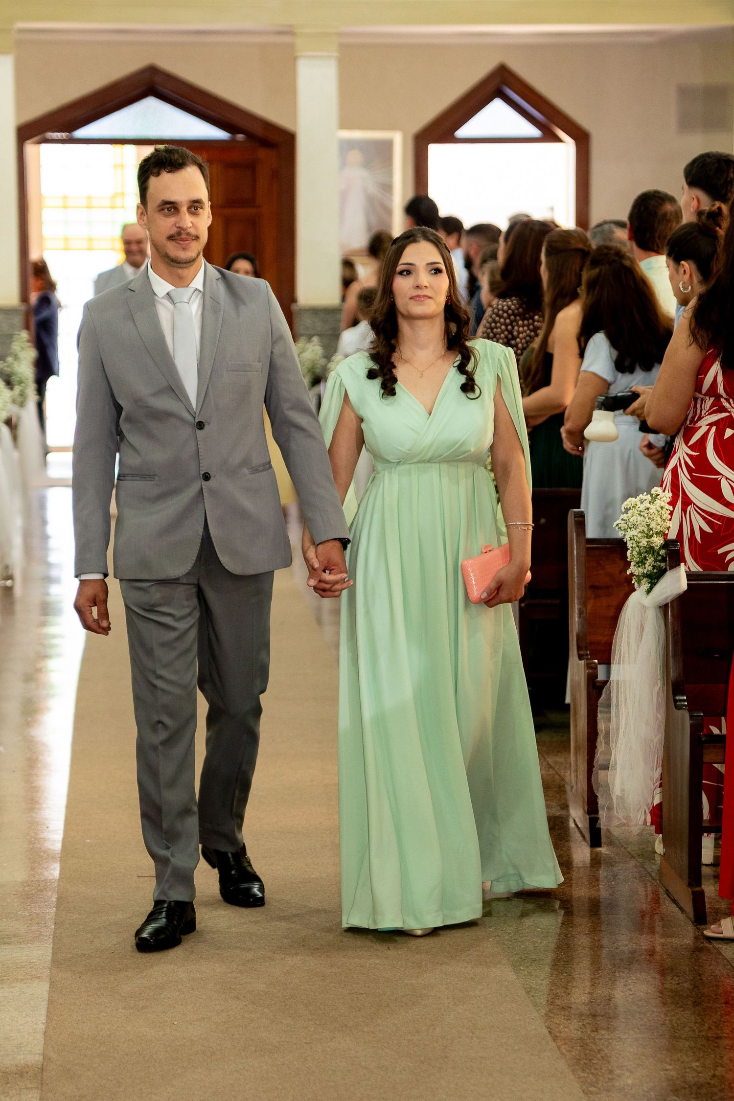 Couple walking down church aisle, man in gray suit, woman in mint green gown, holding hands at wedding.