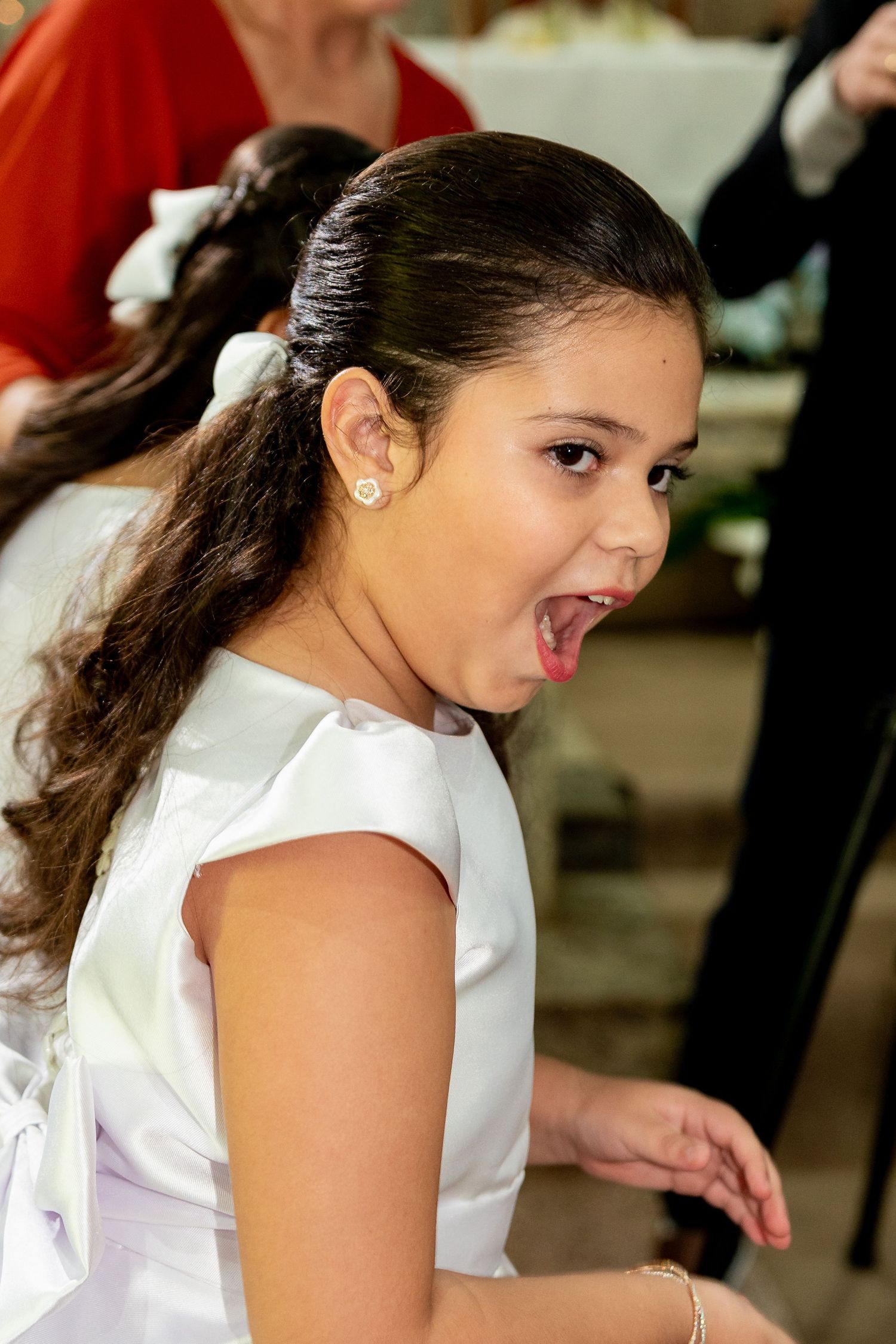 Young girl in white dress with pearl earring, mouth open in excitement at a formal event.