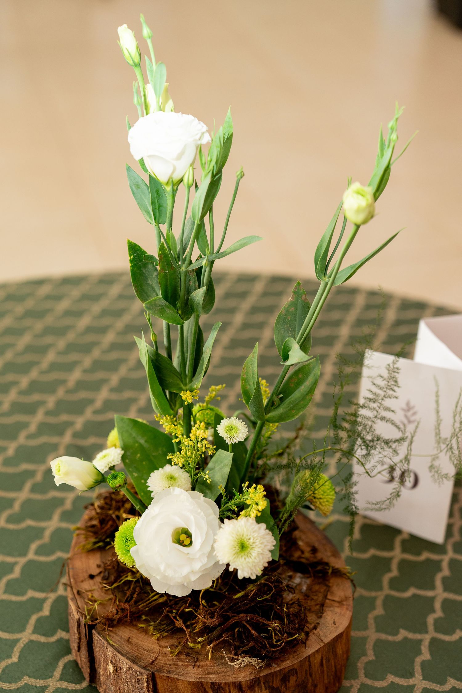White lisianthus and ranunculus floral arrangement on a rustic wood stump centerpiece with green accents.