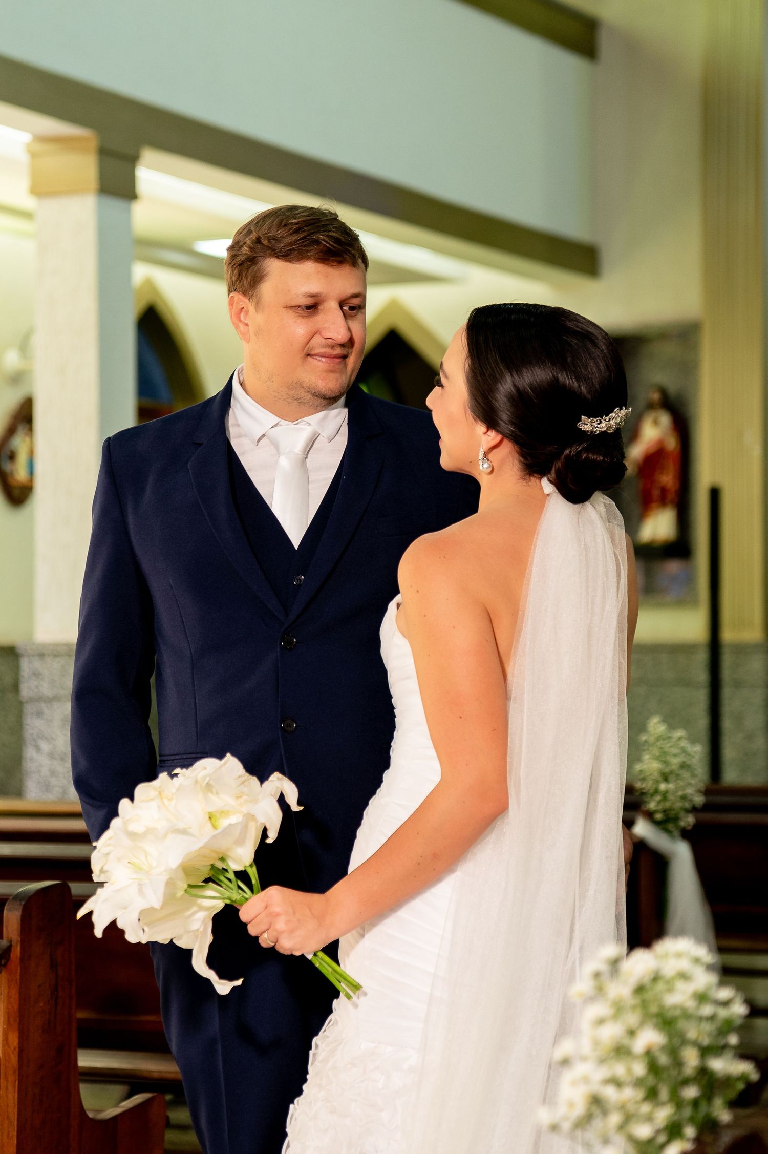 Bride and groom share a romantic moment at the altar, bride holding white calla lily bouquet in a church wedding.