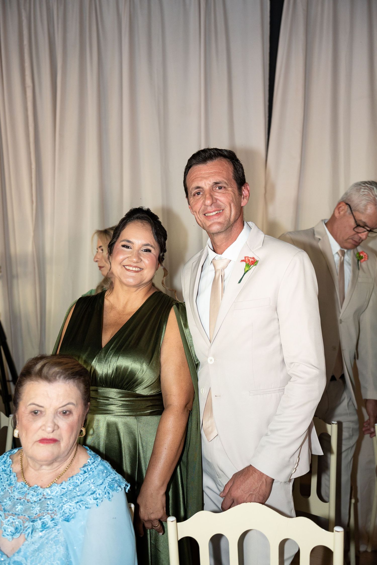 A man in a white suit and a woman in a green dress pose together at a wedding reception.