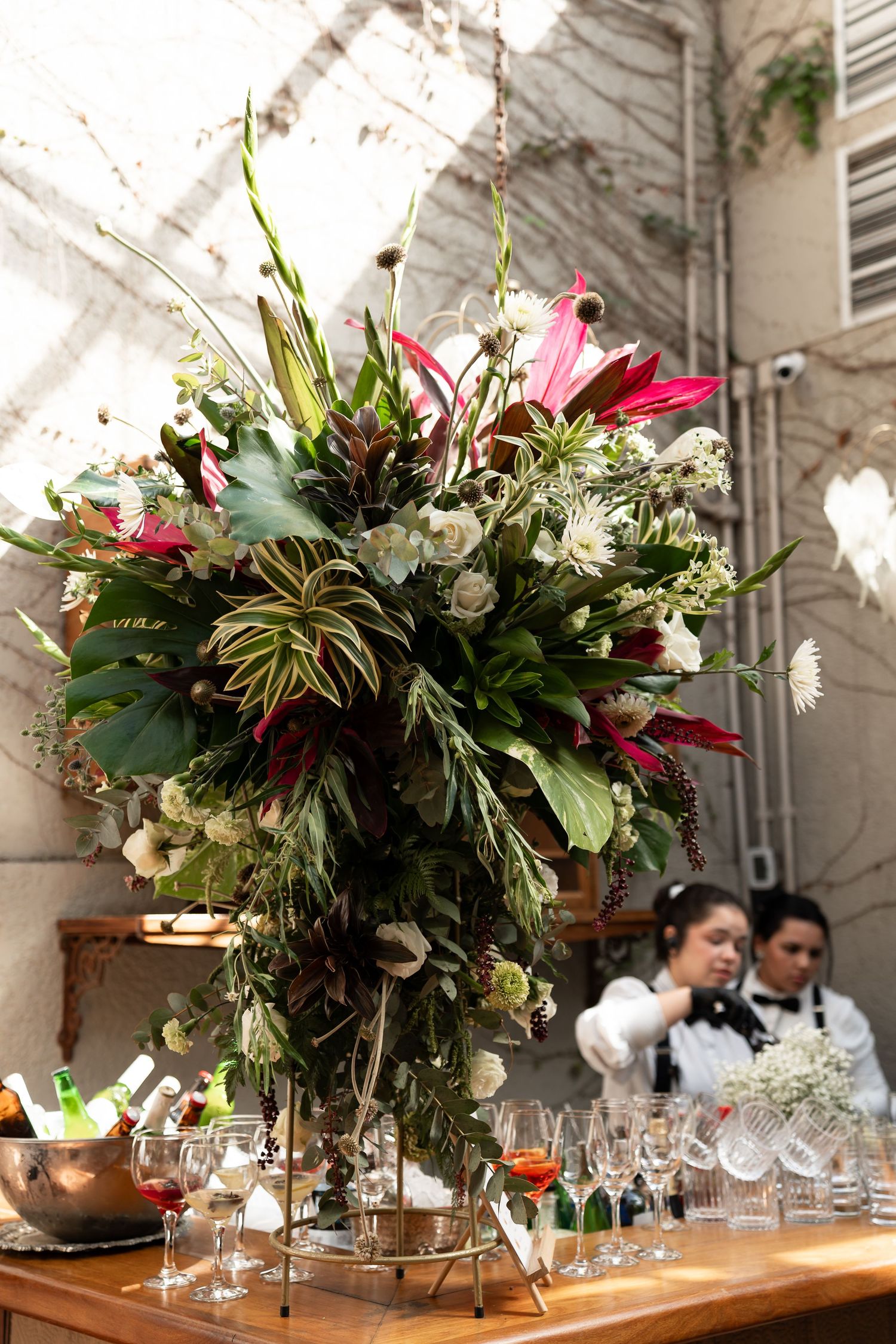 Lush floral arrangement with tropical leaves and pink blooms on a bar table with glassware at an elegant event.
