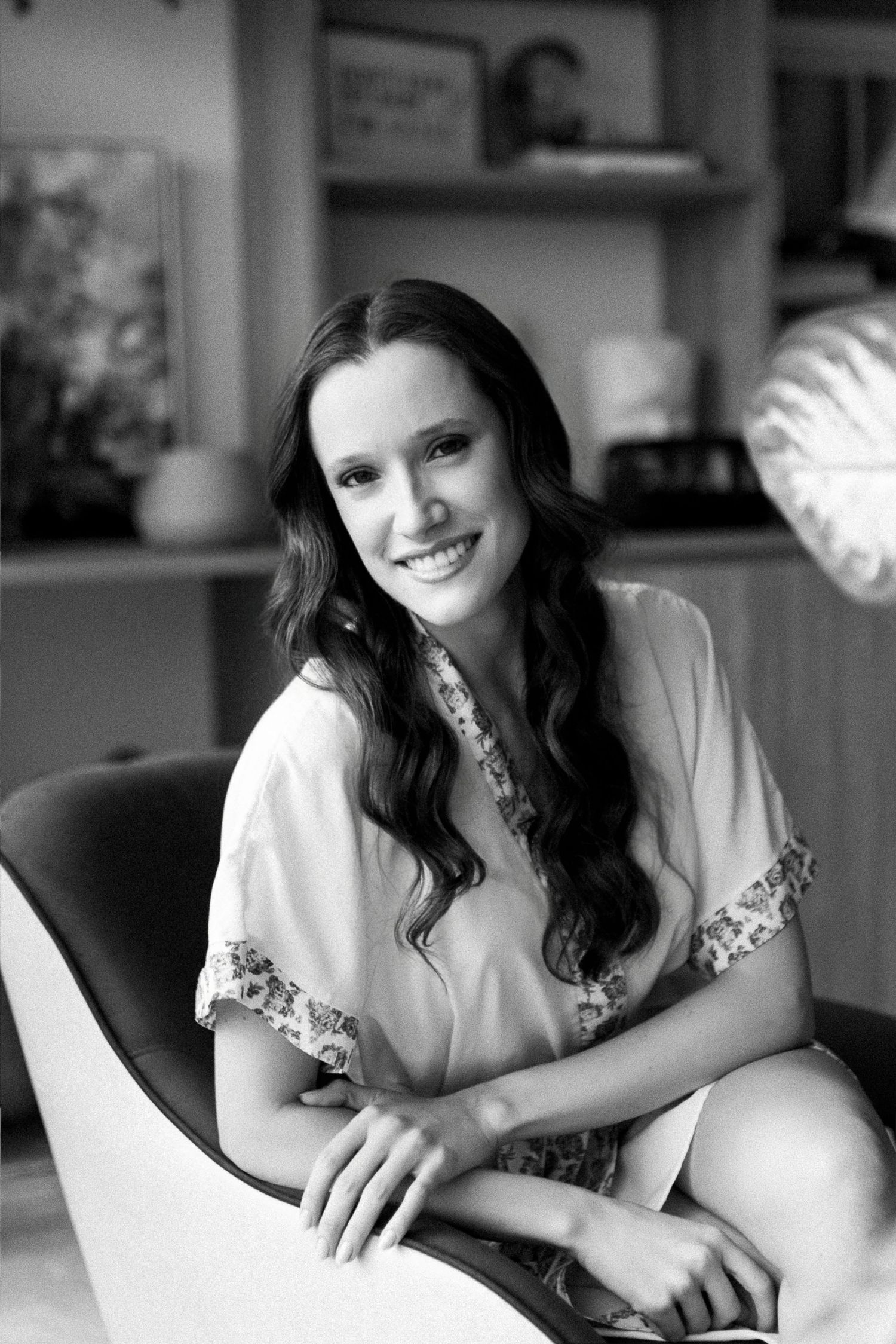 Smiling woman with long dark hair sitting in a modern chair in a stylish room, black and white portrait photo.