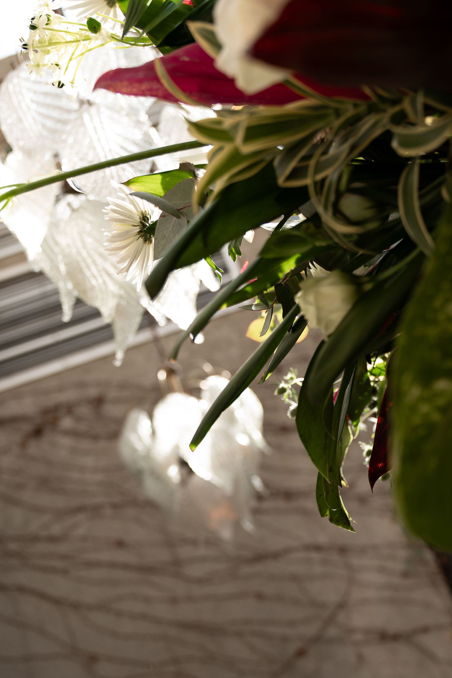 Close-up of a floral arrangement with white blooms and green stems casting shadows on a marble surface.