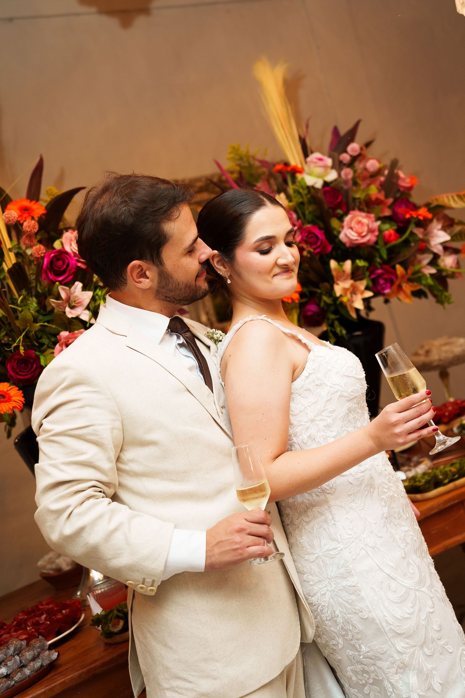 Bride and groom sharing a romantic toast with champagne glasses, surrounded by colorful floral arrangements at their wedding reception.