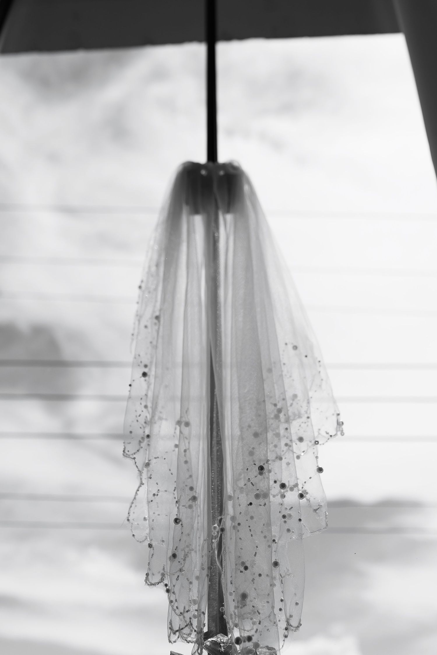 Black and white photo of a delicate beaded bridal veil hanging elegantly, adorned with scattered crystal embellishments.