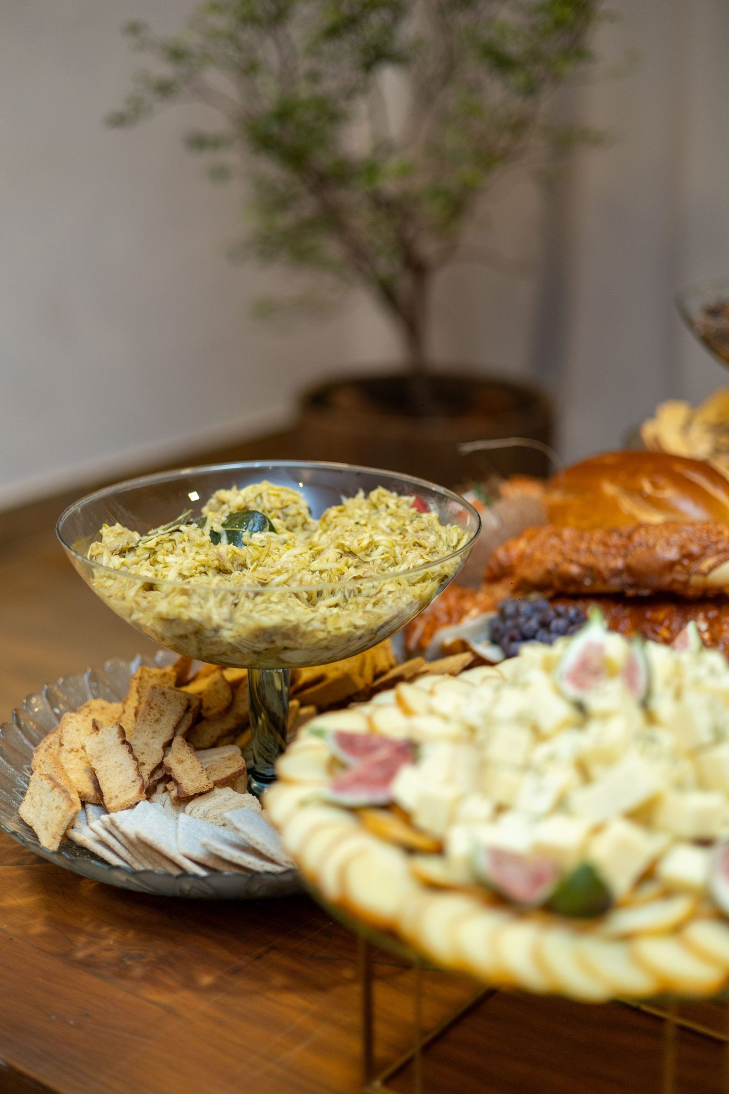 Elegant charcuterie spread with dips, crackers, sliced meats, and pastries on a wooden table.